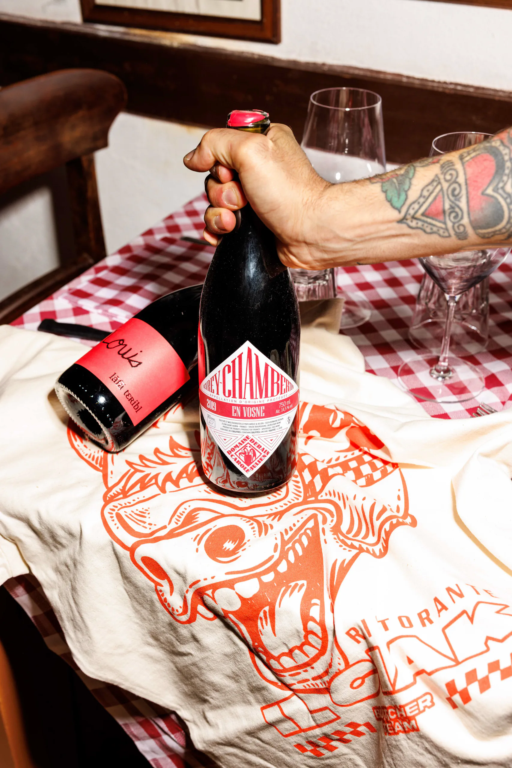 Hand setting a bottle of sparkling wine on a red-checkered tablecloth with wine glasses at Il Ciak, Rome, Italy
