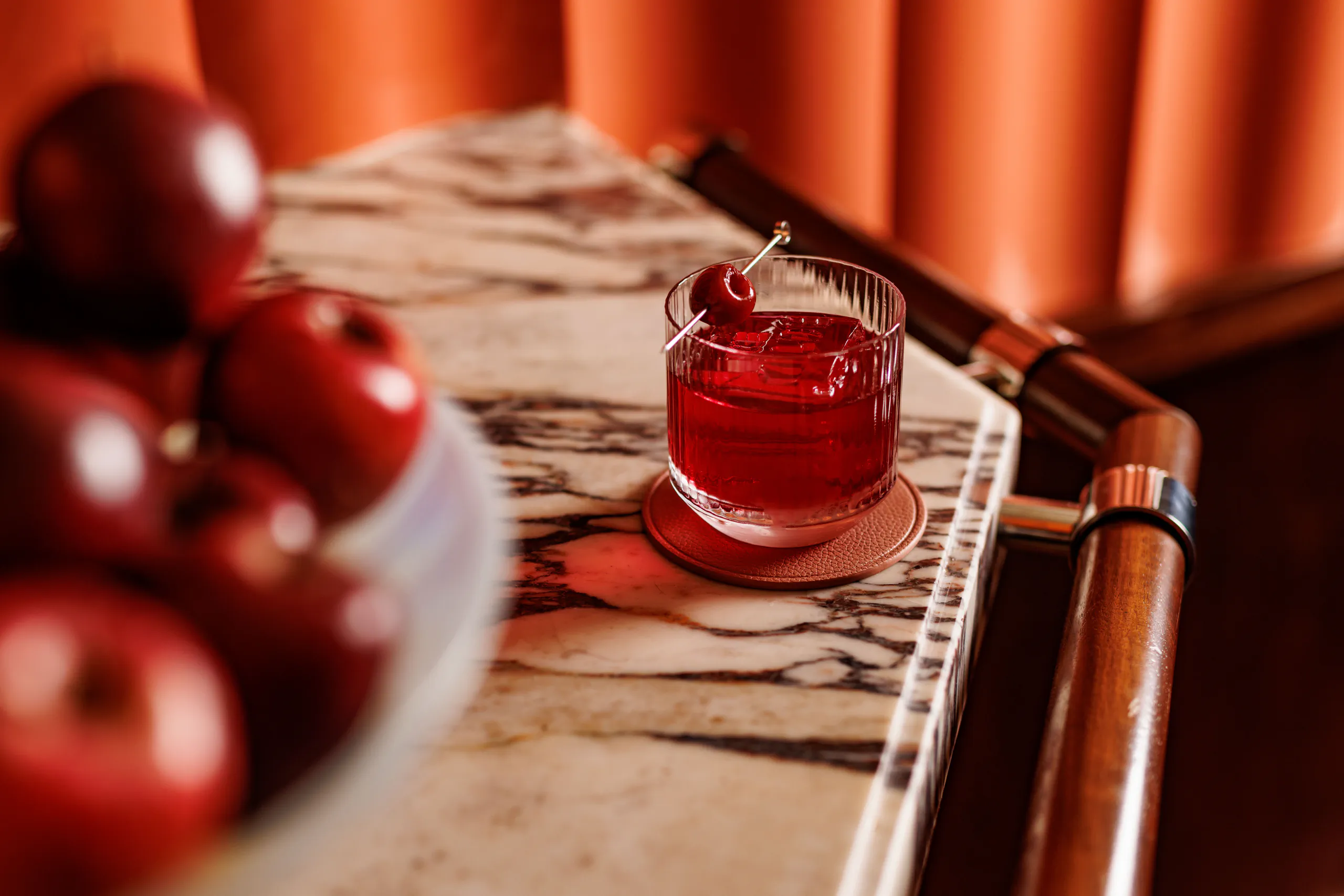 Red cocktail on a marble bar cart beside a bowl of red apples at The Wilde, Milan, Italy