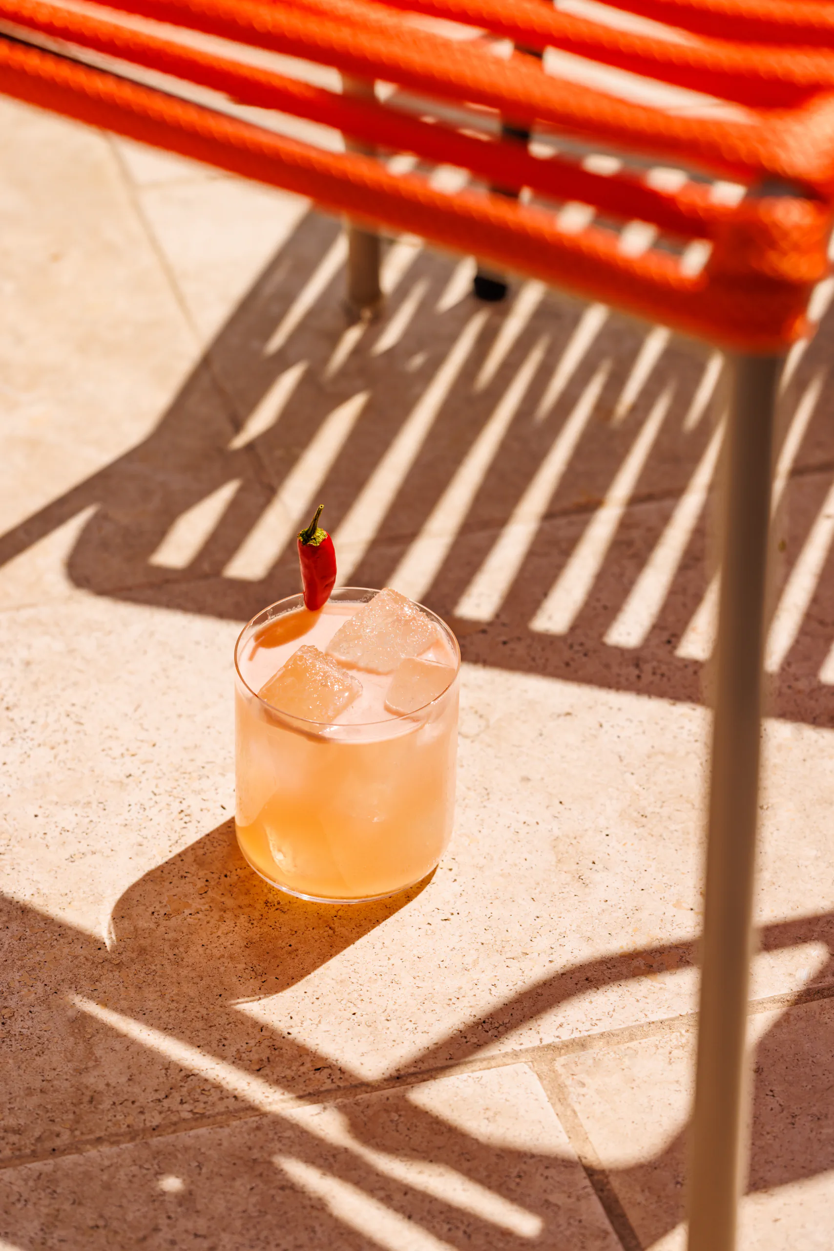 Orange cocktail with a chili garnish on a sunny terrace beside orange chairs