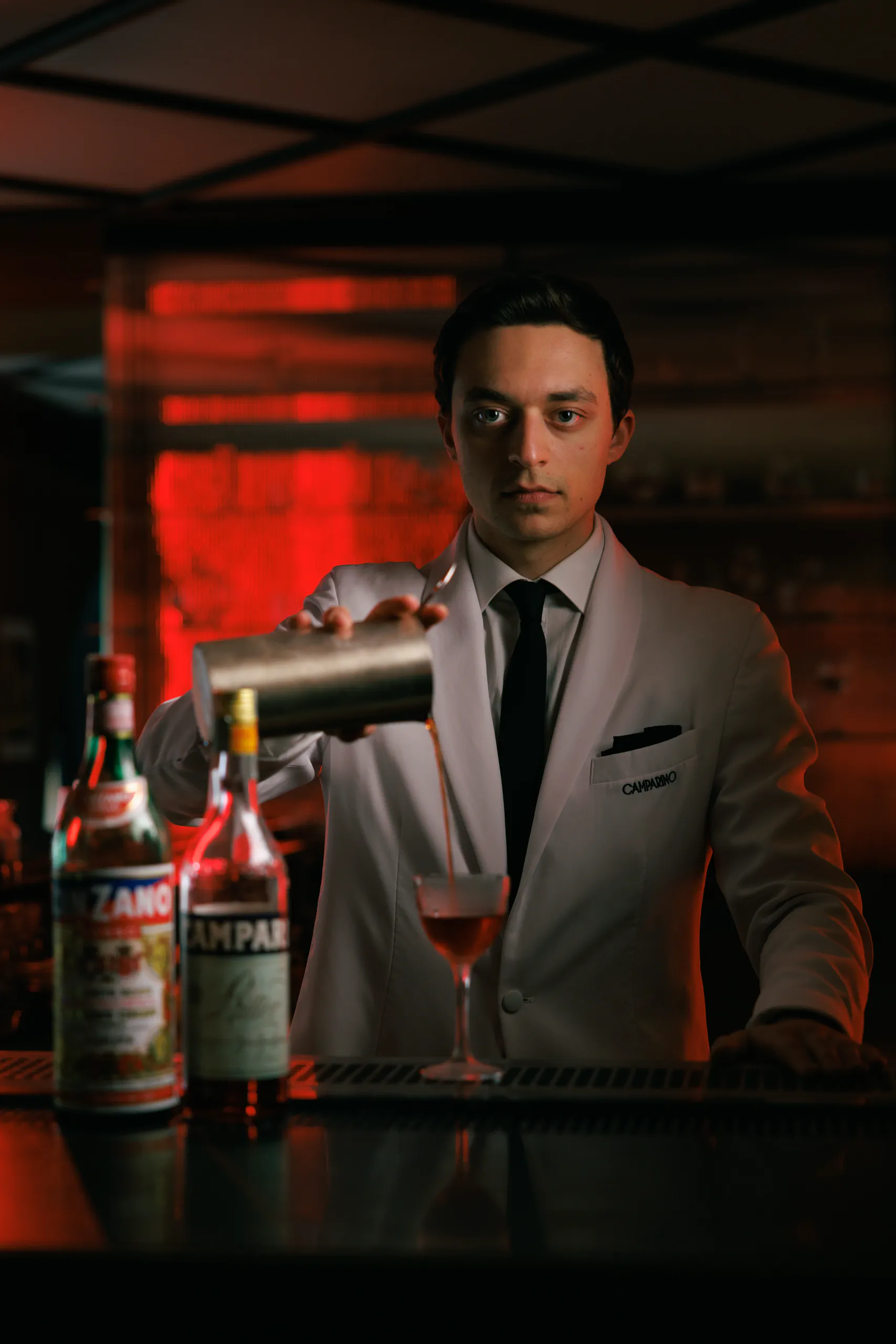 Bartender in a grey suit pouring a red cocktail at a moody red-lit bar at Camparino in galleria, Milan, Italy