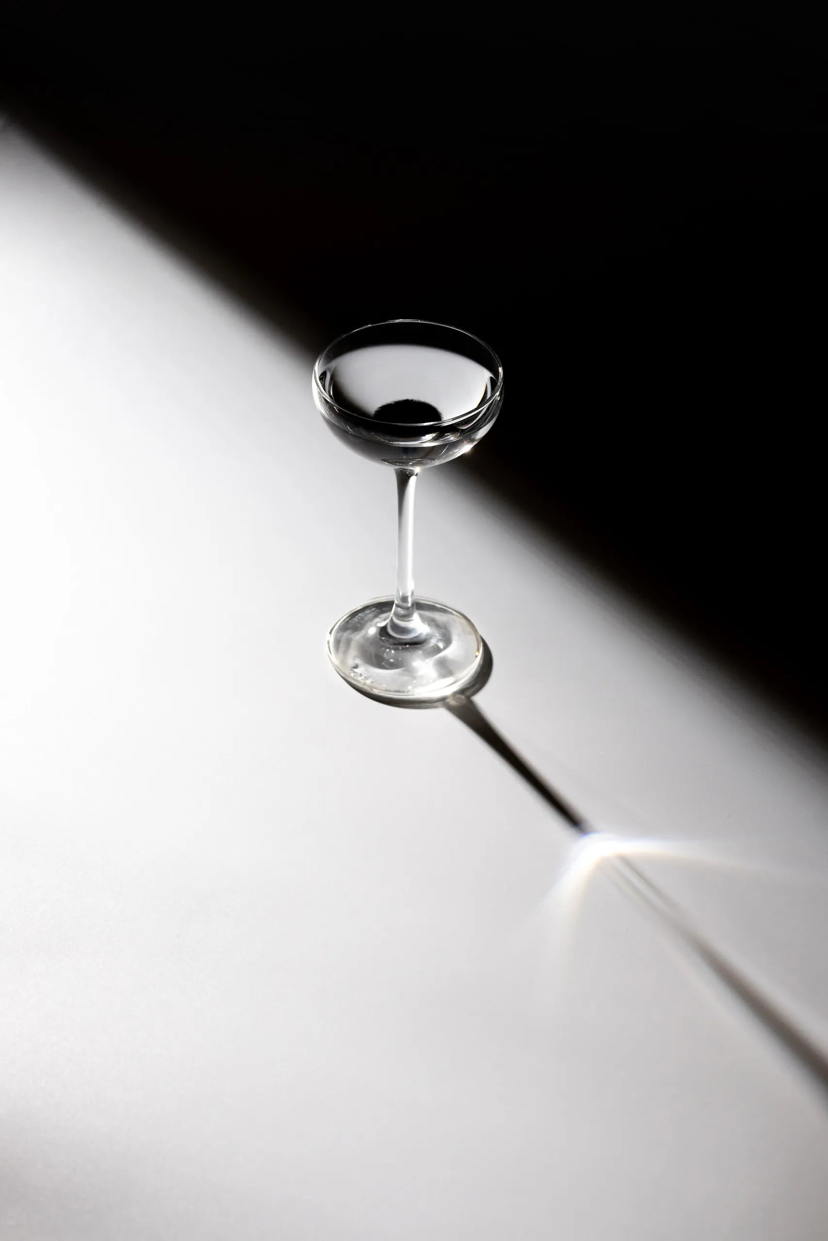 Dark cocktail in a coupe glass with a bar spoon on a bright white surface