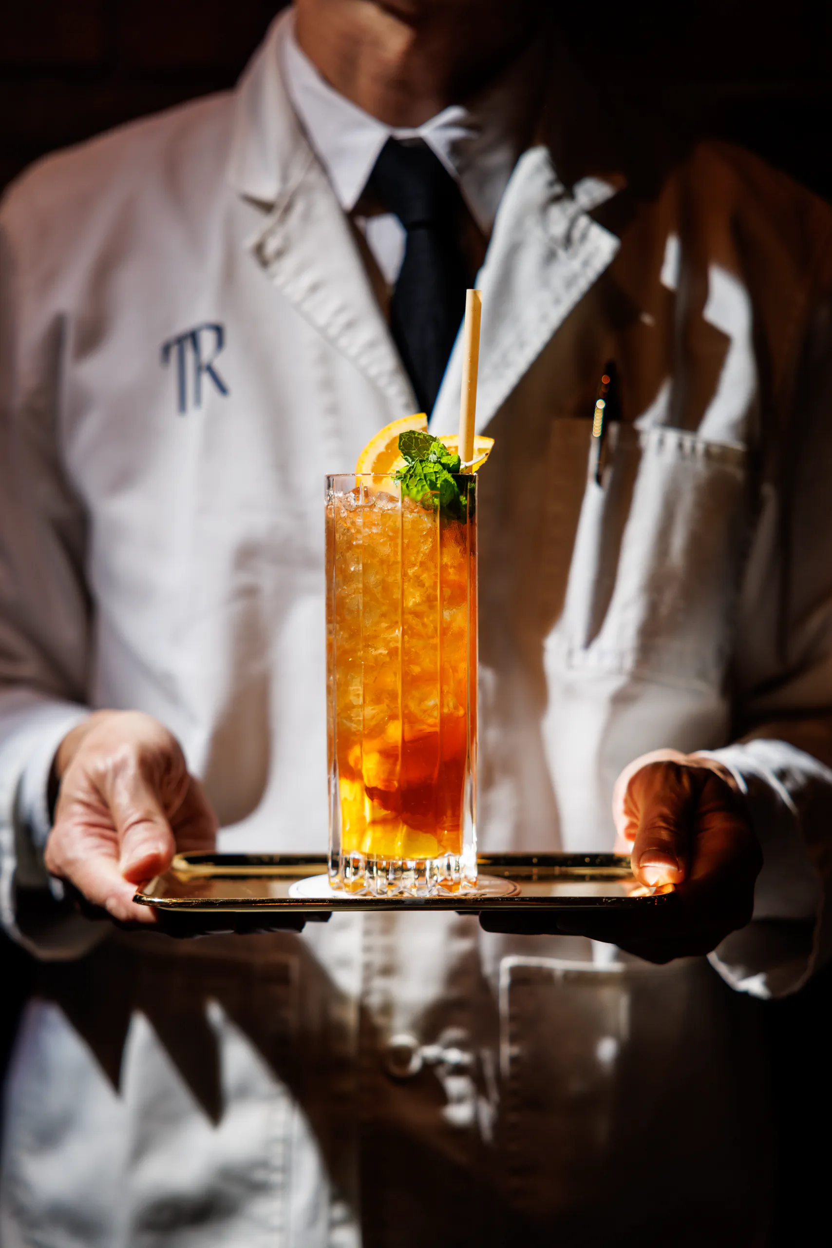 Waiter holding a tray with a tall garnished cocktail at Trench Bar in Tokyo, Japan