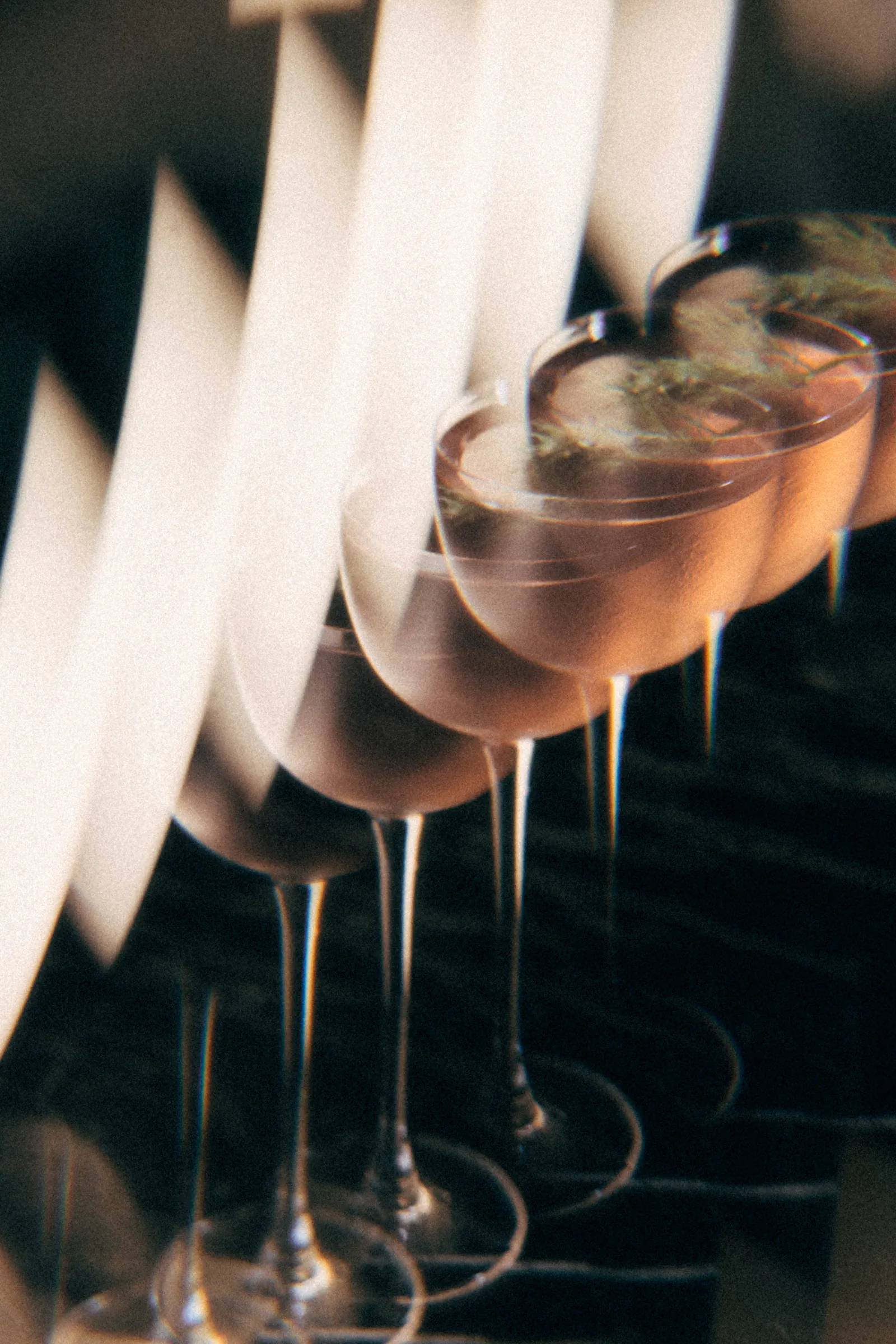 Row of coupe cocktails lined up along a bar in low light