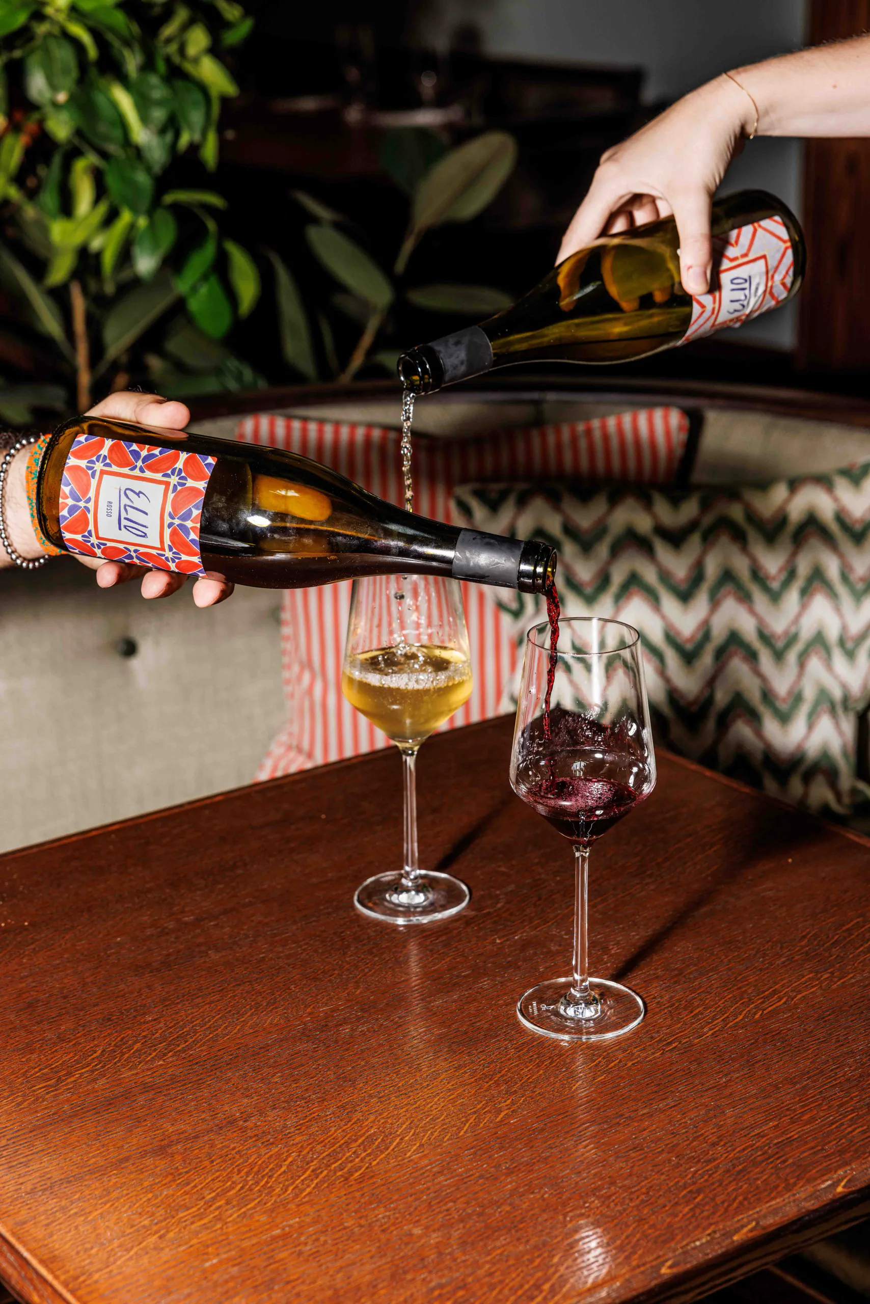 Hand pouring white wine into glasses on a wooden table in a natural-wine bar