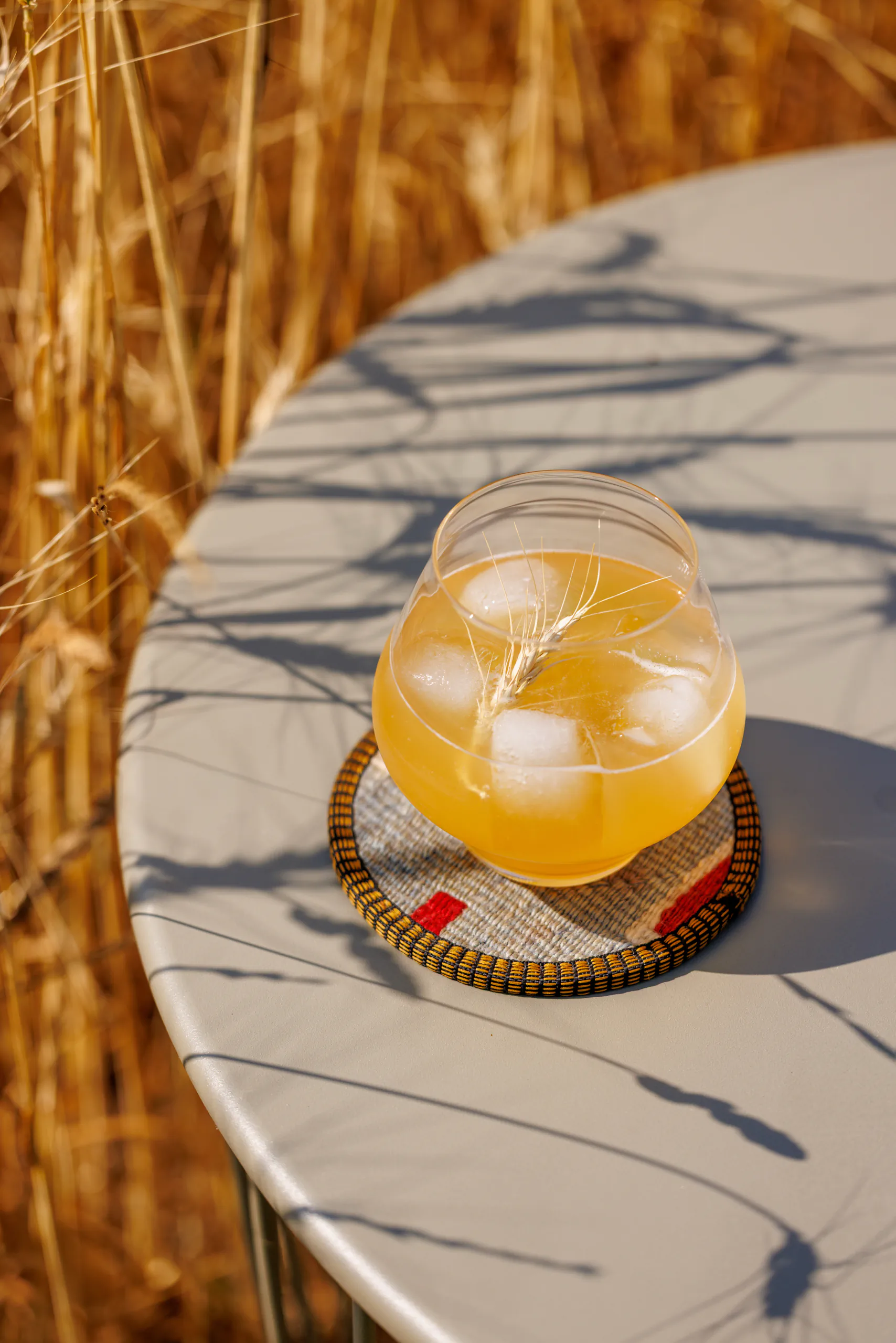 Orange cocktail over ice on a marble bistro table outdoors near dry reeds