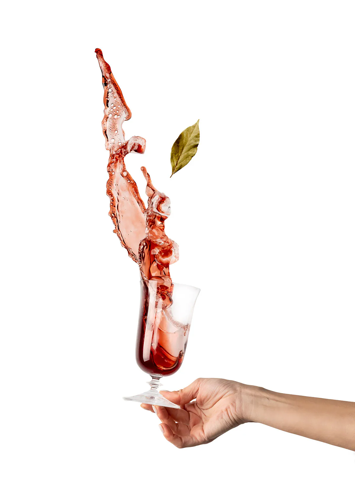 Hand holding a glass of red wine splashing out with a bay leaf, on white