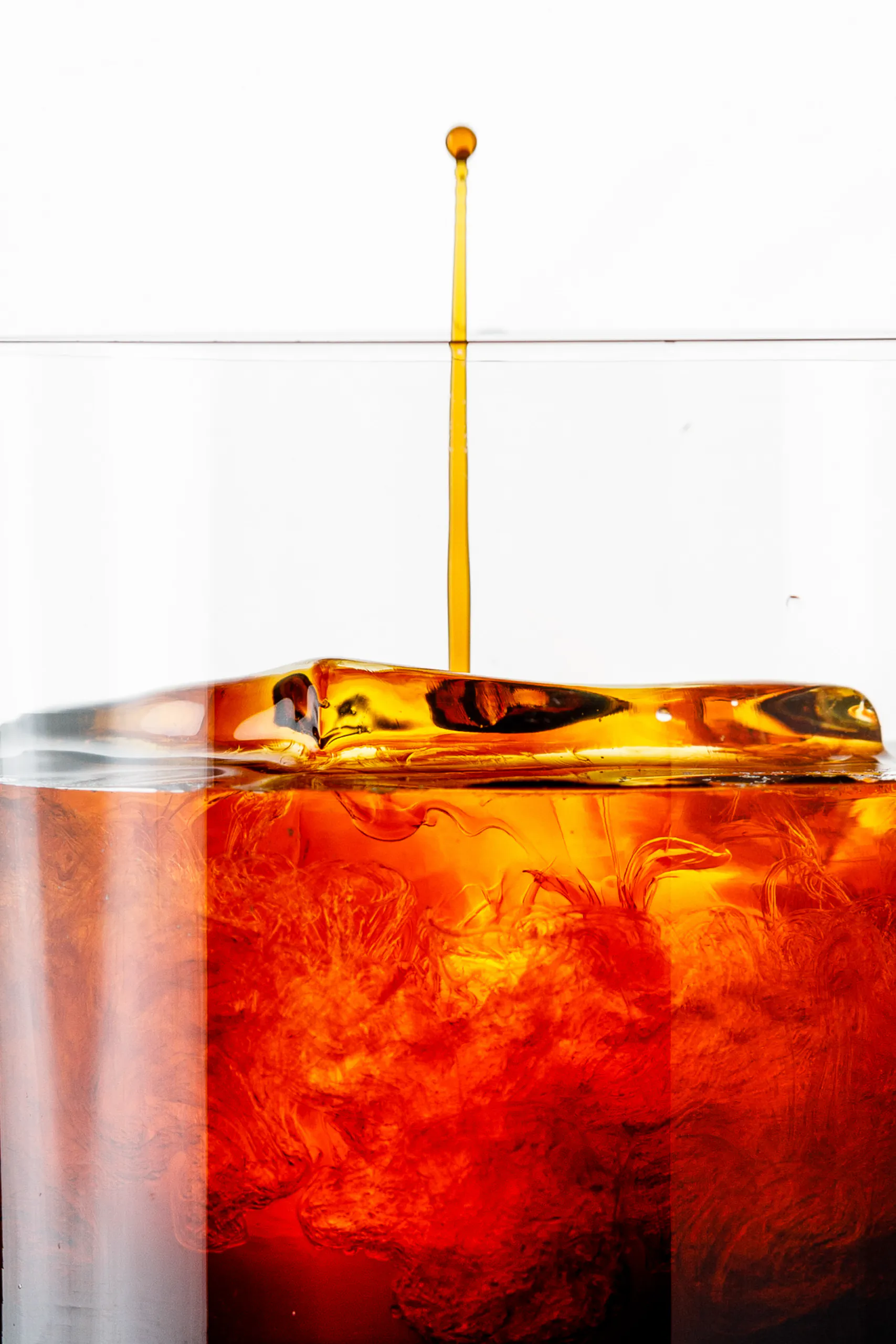 Close-up of a drop falling into an amber aperitif over ice