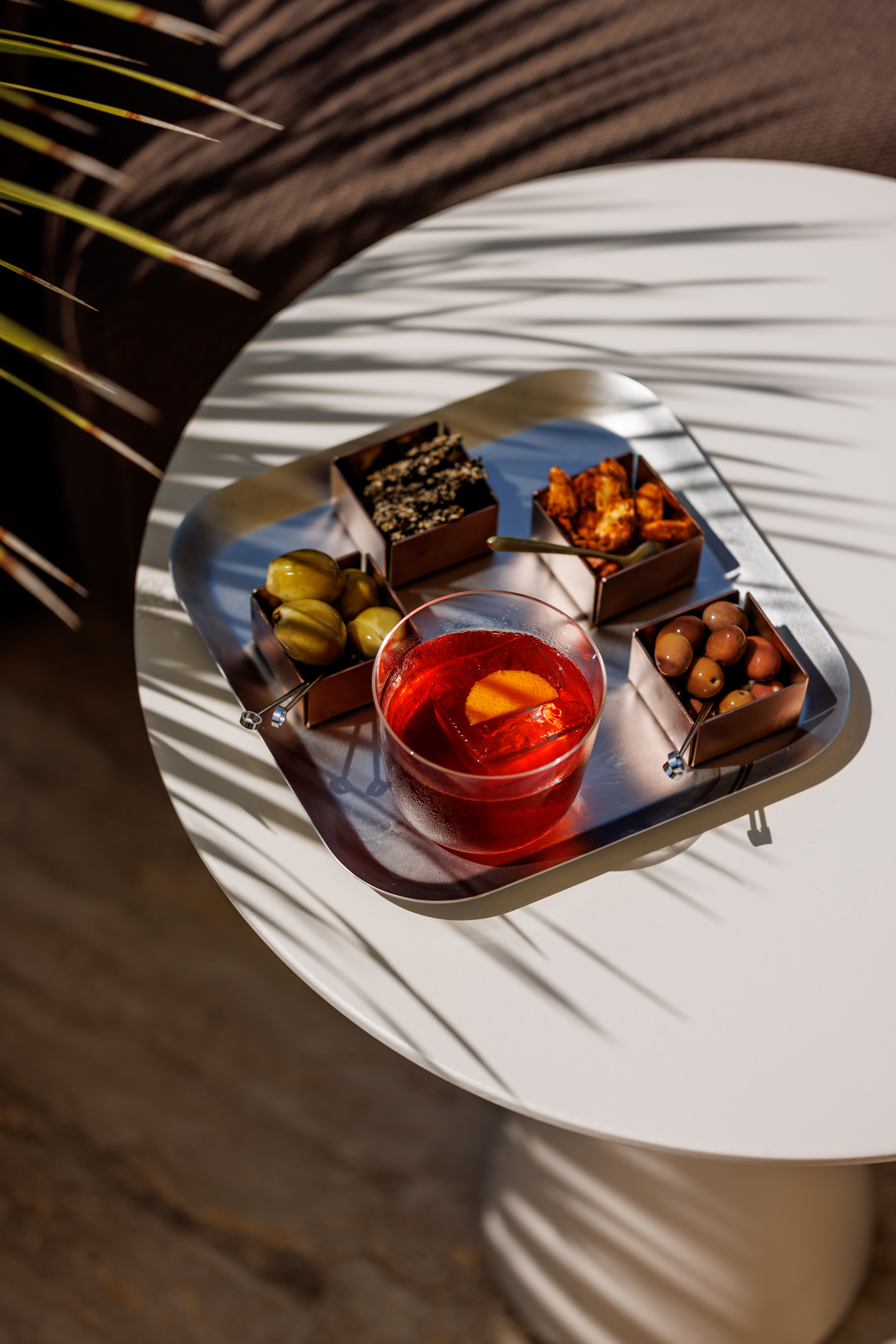 Tray of chocolates and a red cocktail on a table in dappled palm-leaf shadow
