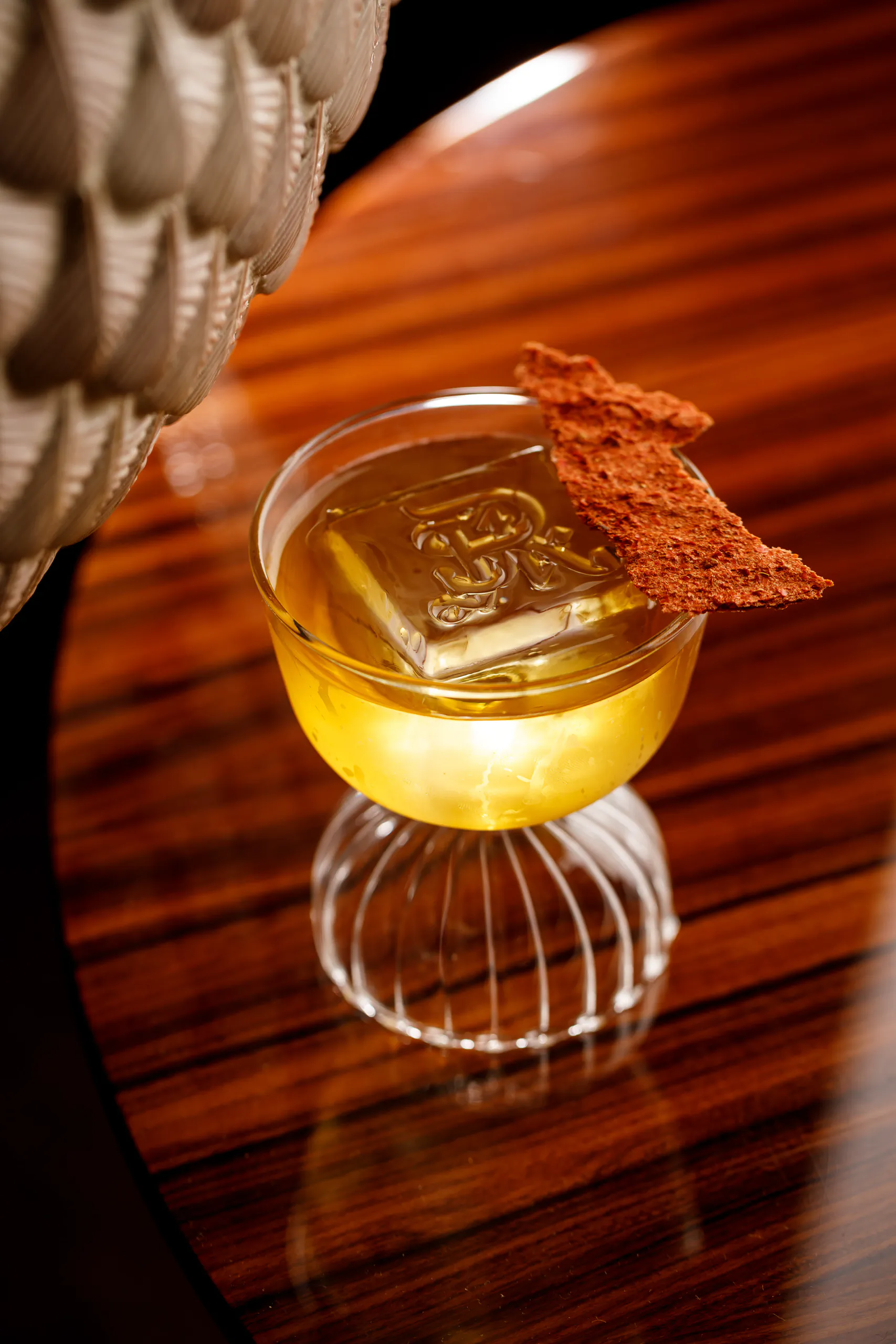 Cocktail in a footed glass with a stamped ice cube and a wafer garnish