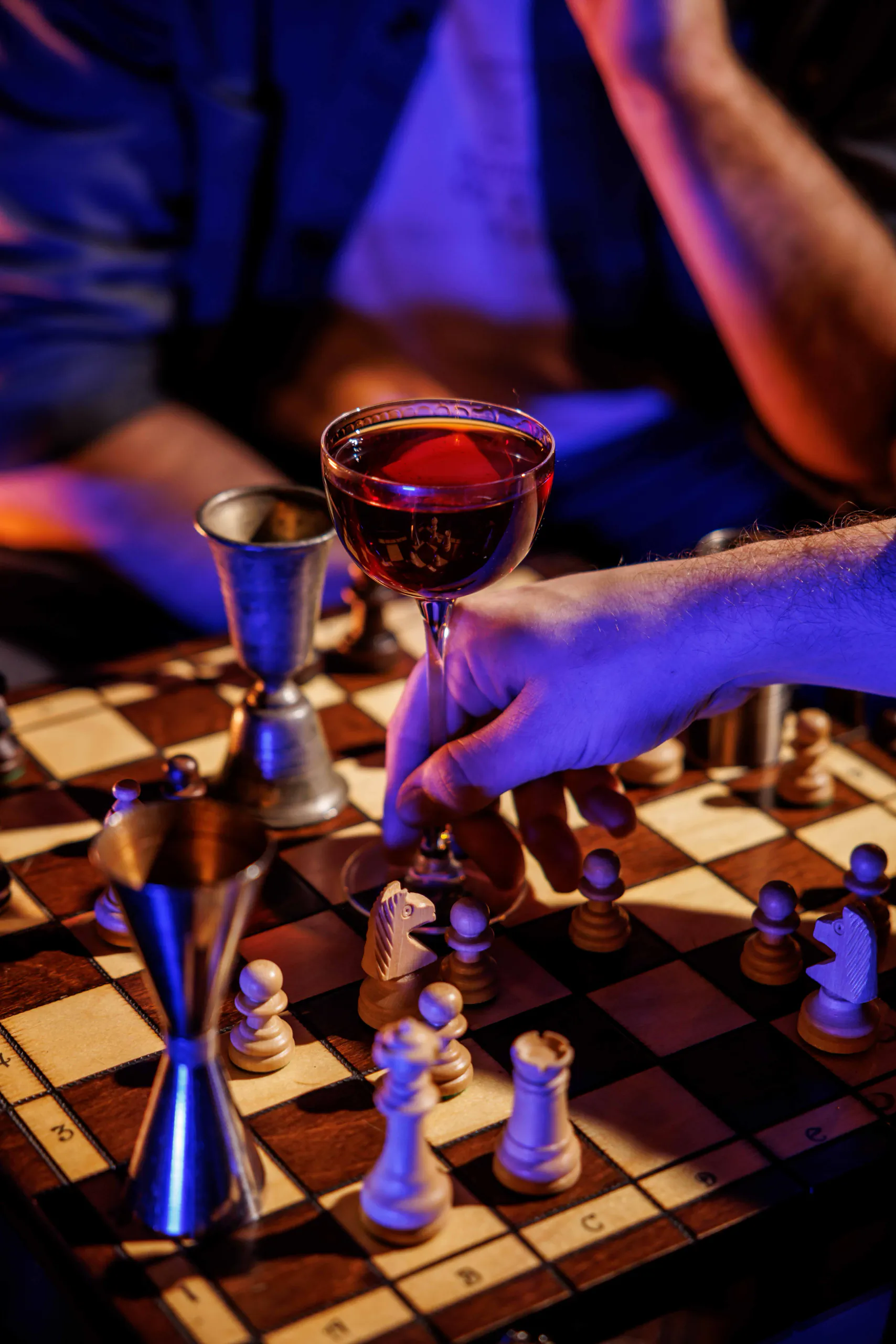 Hand reaching for a red cocktail on a chessboard in a purple-lit bar