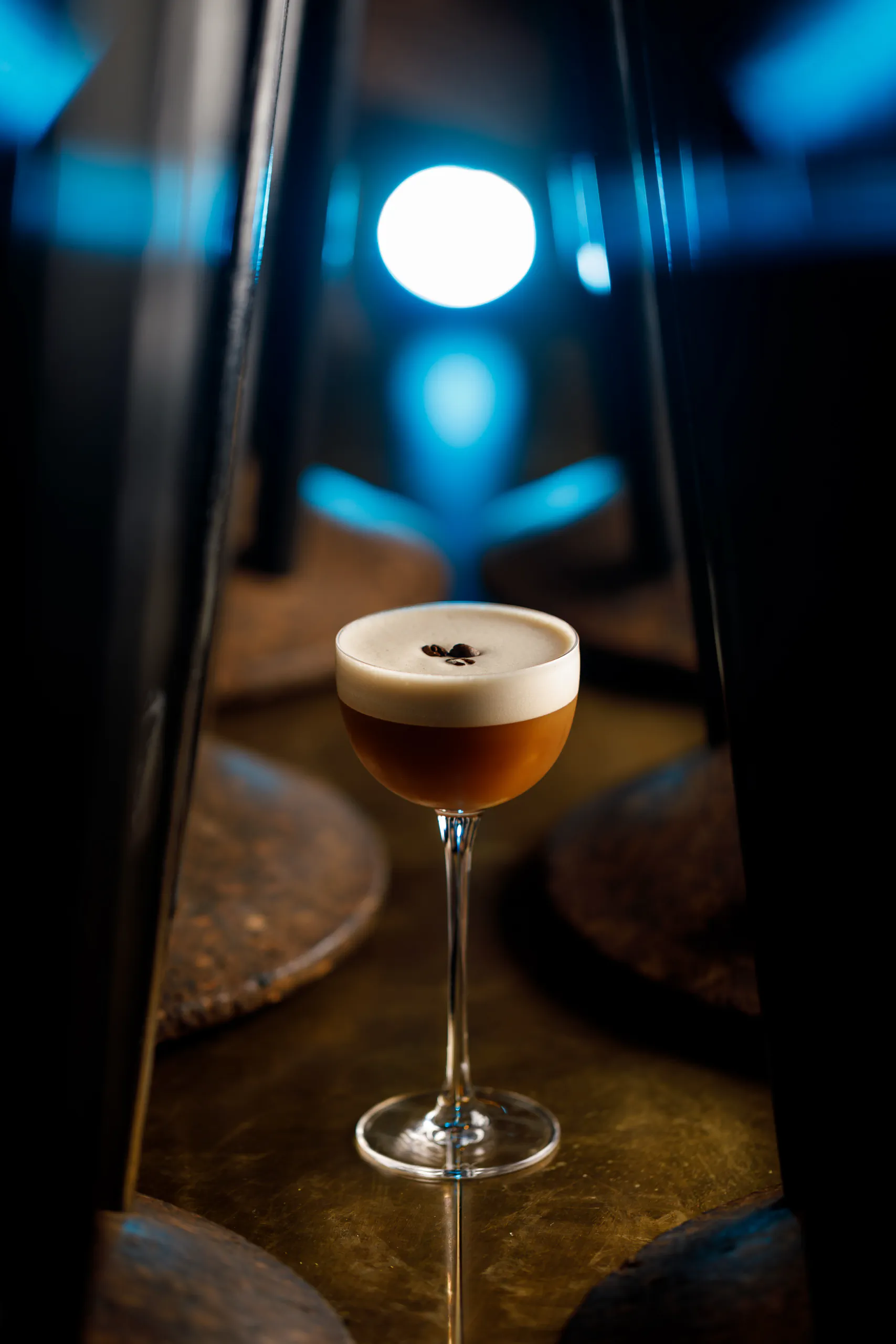 Espresso martini with foam in a coupe glass on a blue-lit bar