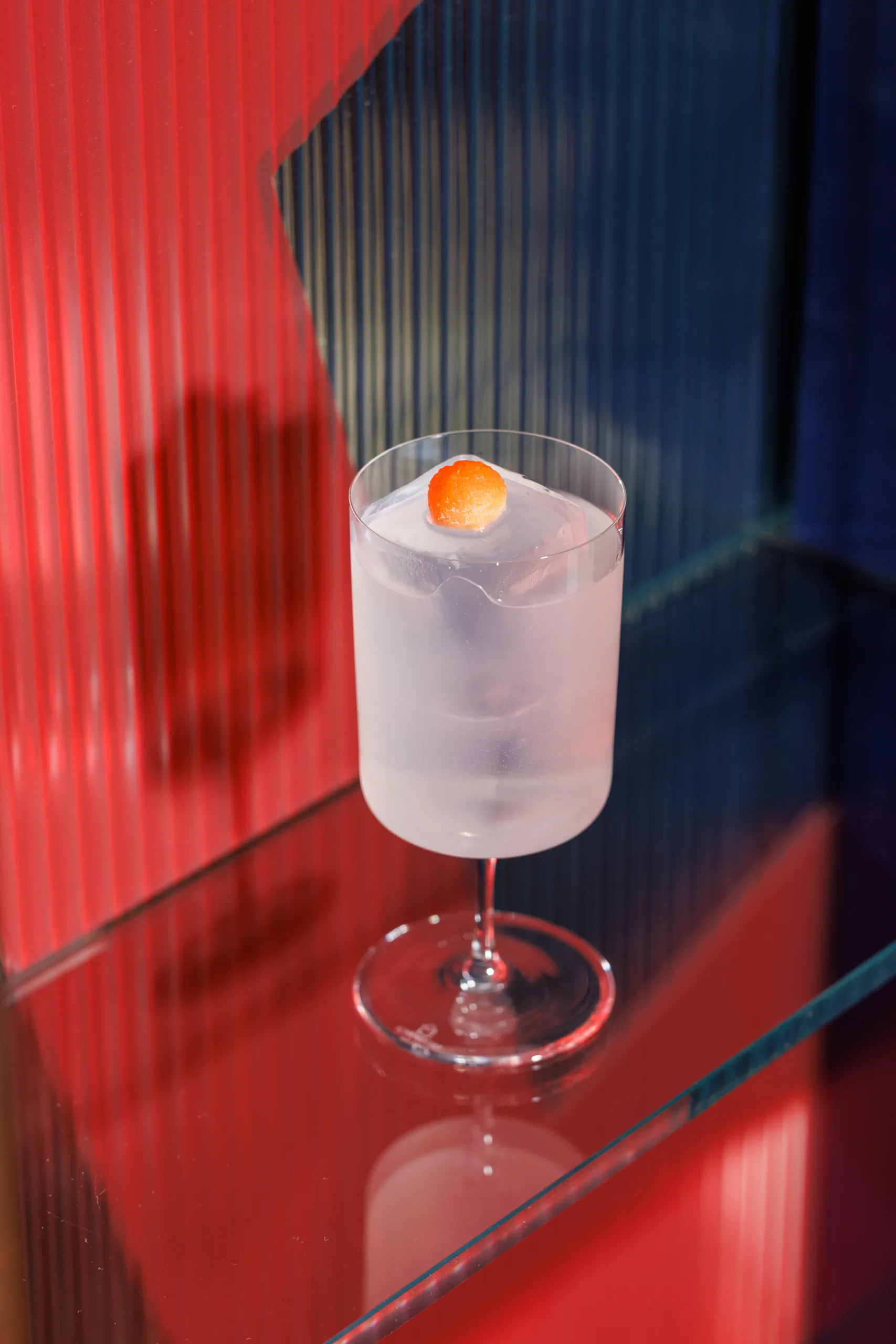 Cloudy pale cocktail with an orange garnish against a red fluted-glass background — Camparino in Galleria, Milan