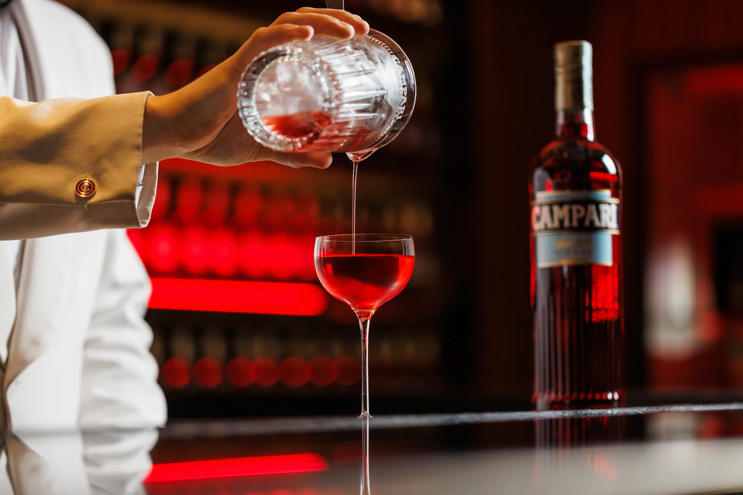 Bartender straining a red cocktail into a coupe beside a Campari bottle — Camparino in Galleria, Milan