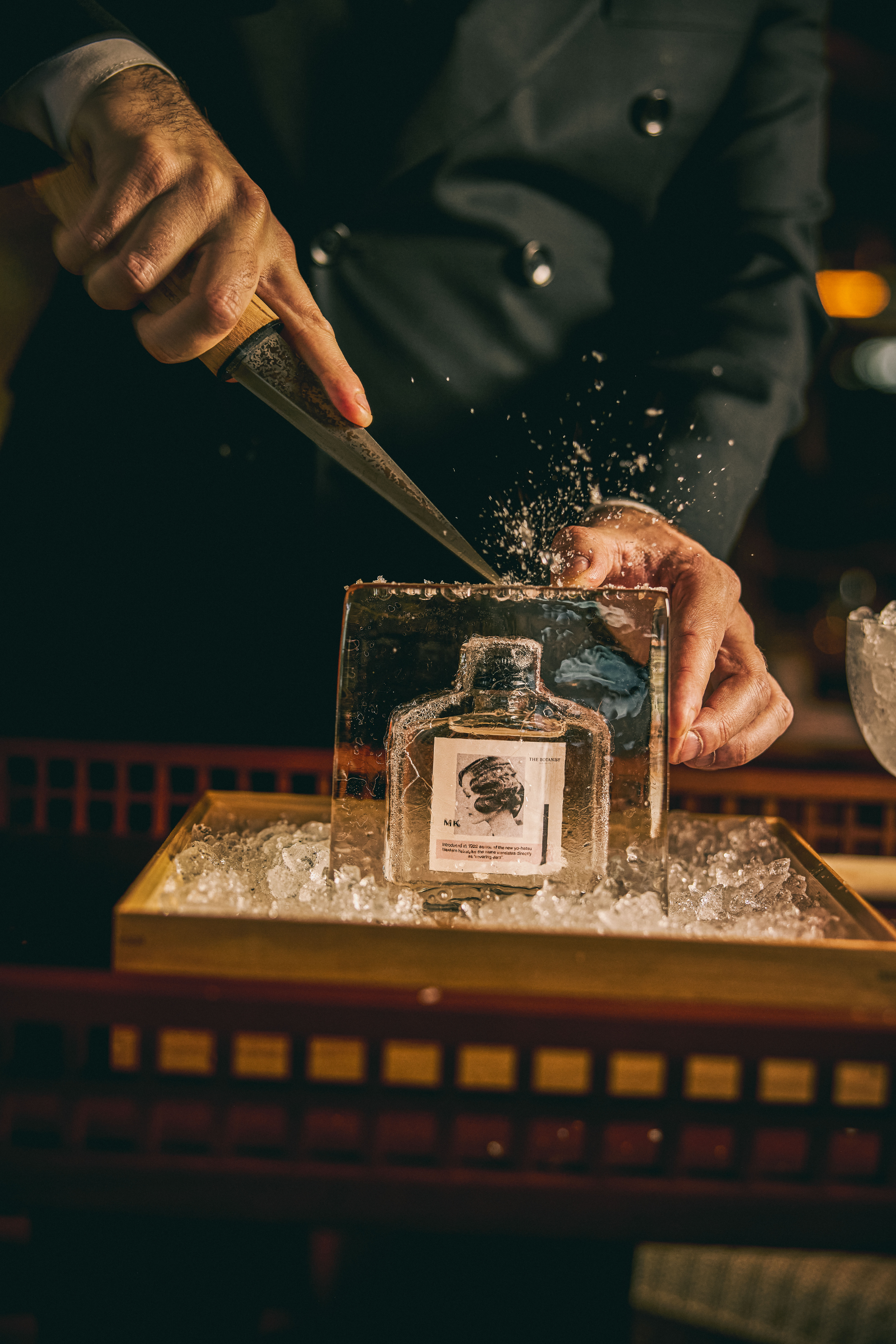 Bartender chipping a block of clear ice with an ice pick beside a gin Martini bottle at a bar station — Mimi Kakushi, Delano, Miami