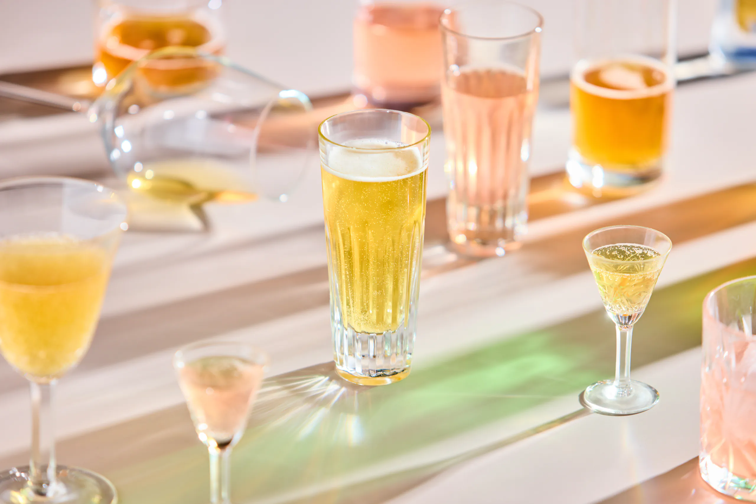 Row of sparkling cocktails lined up along a bar in colourful light — kombucha