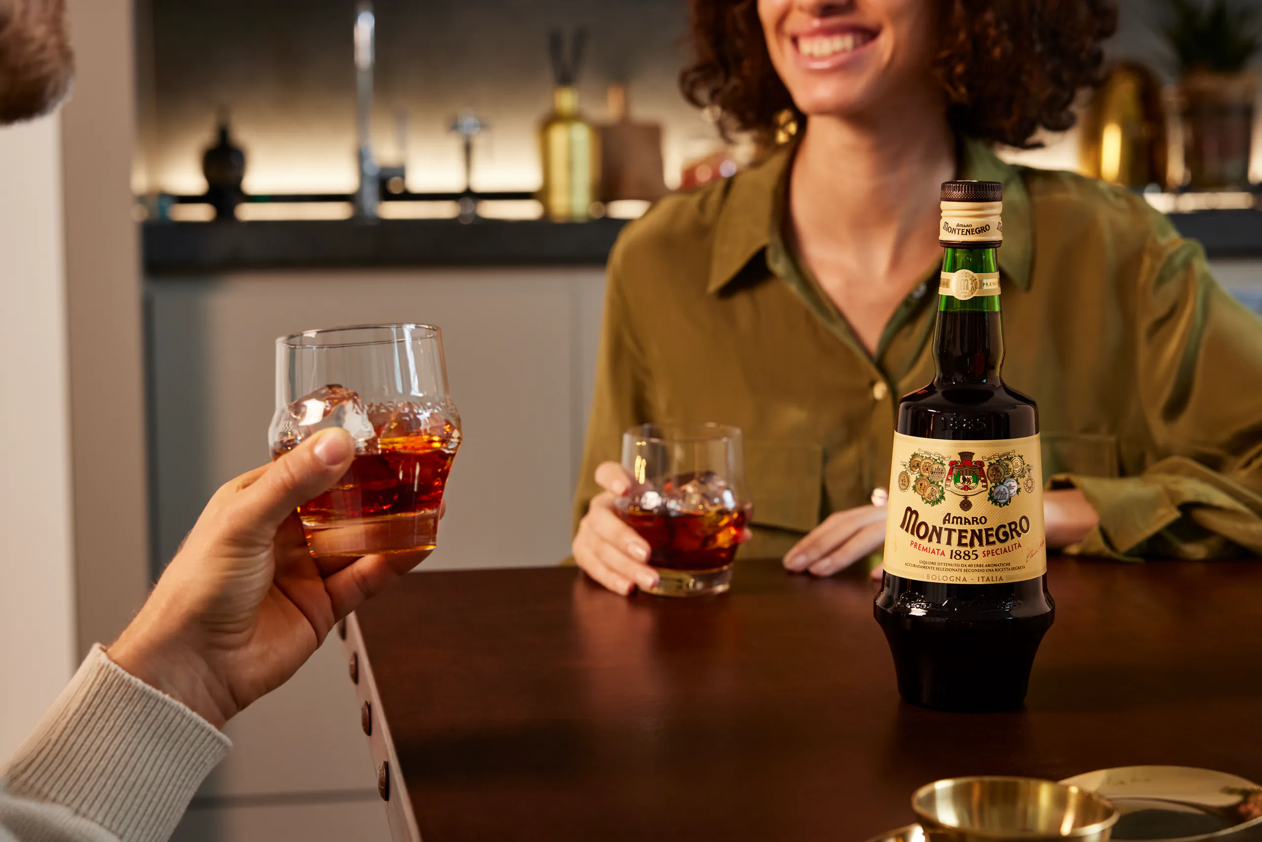 Woman smiling at a bar with a cocktail beside a bottle of Amaro Montenegro