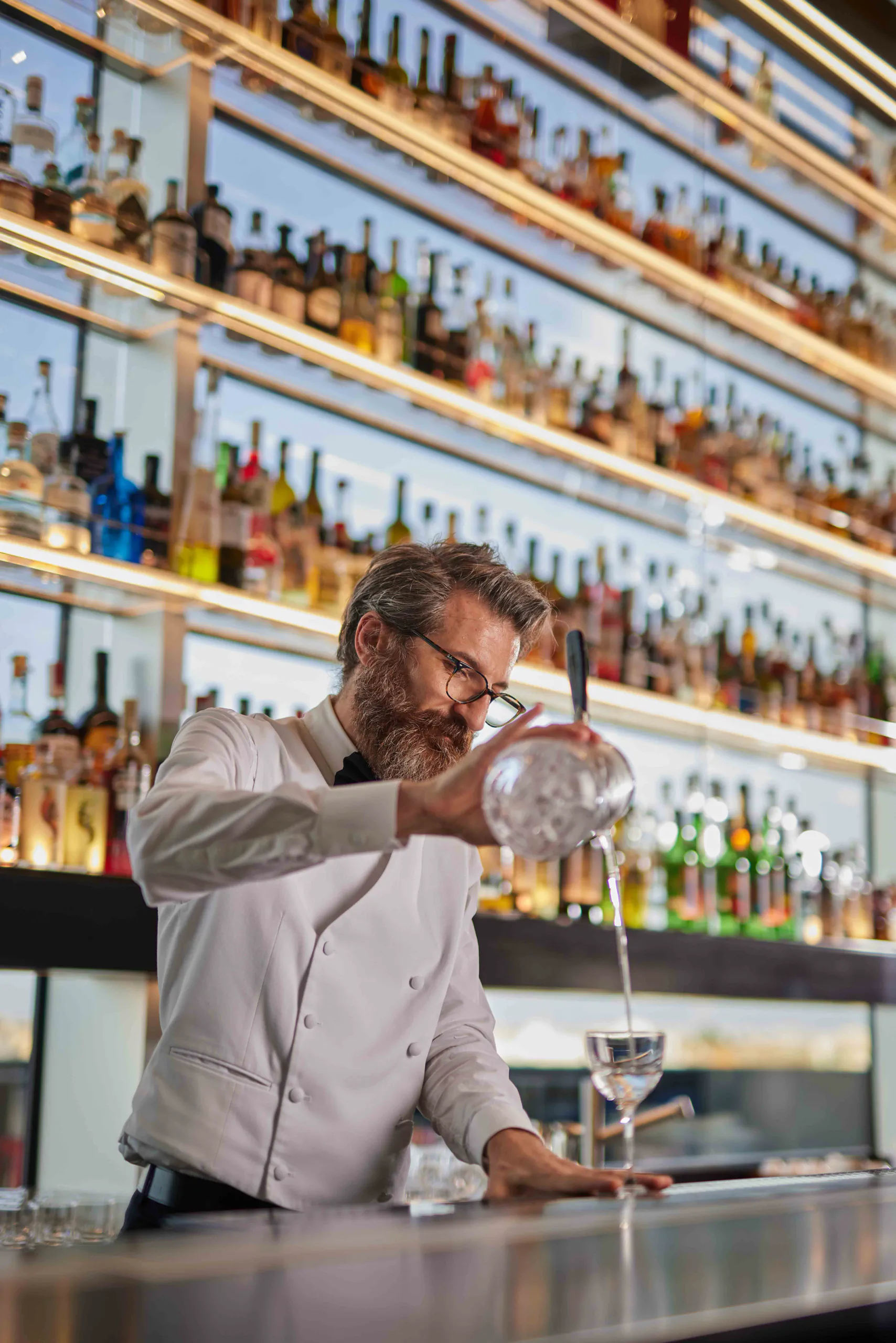 Bartender straining a cocktail behind a well-stocked bar — Torre, Fondazione Prada, Milan