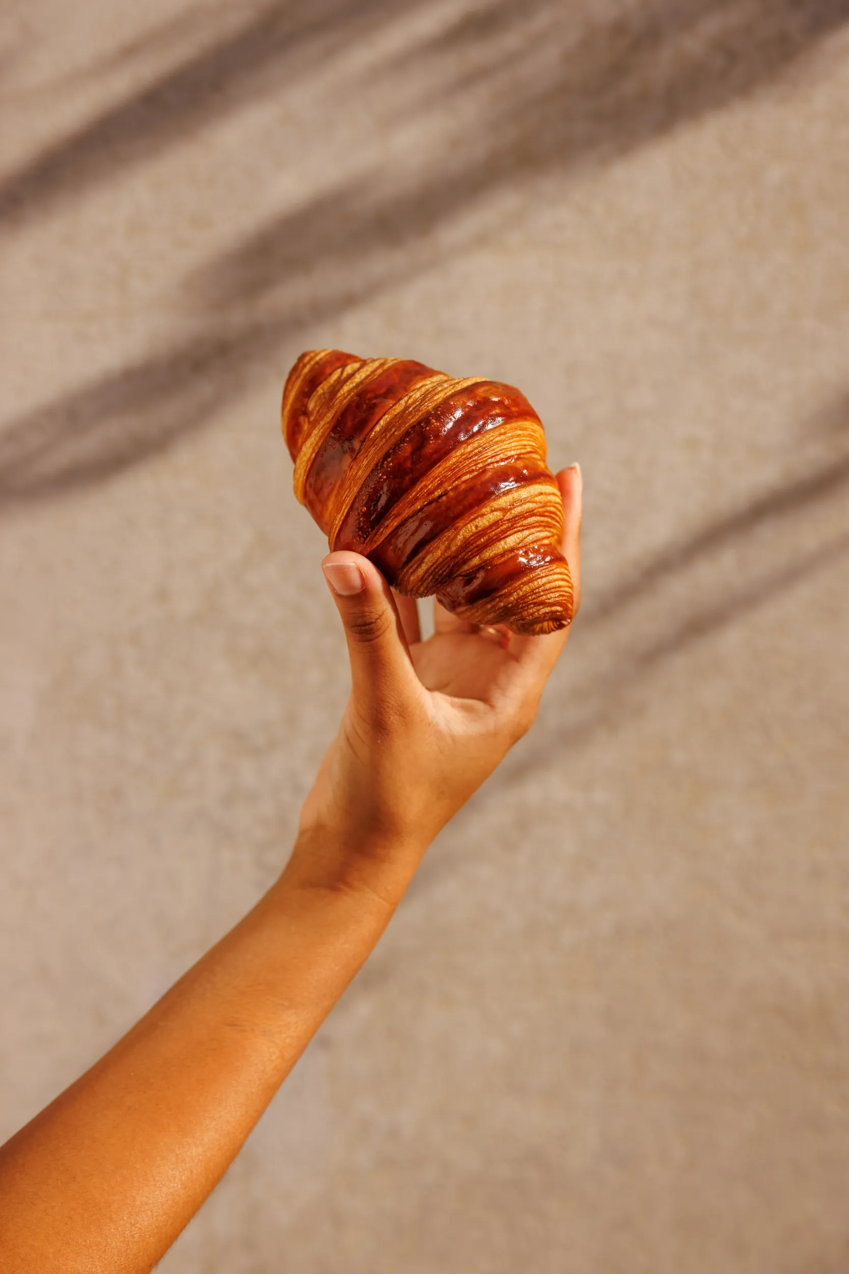 Hand holding a golden croissant in warm sunlight - Mary, Rome, Italy