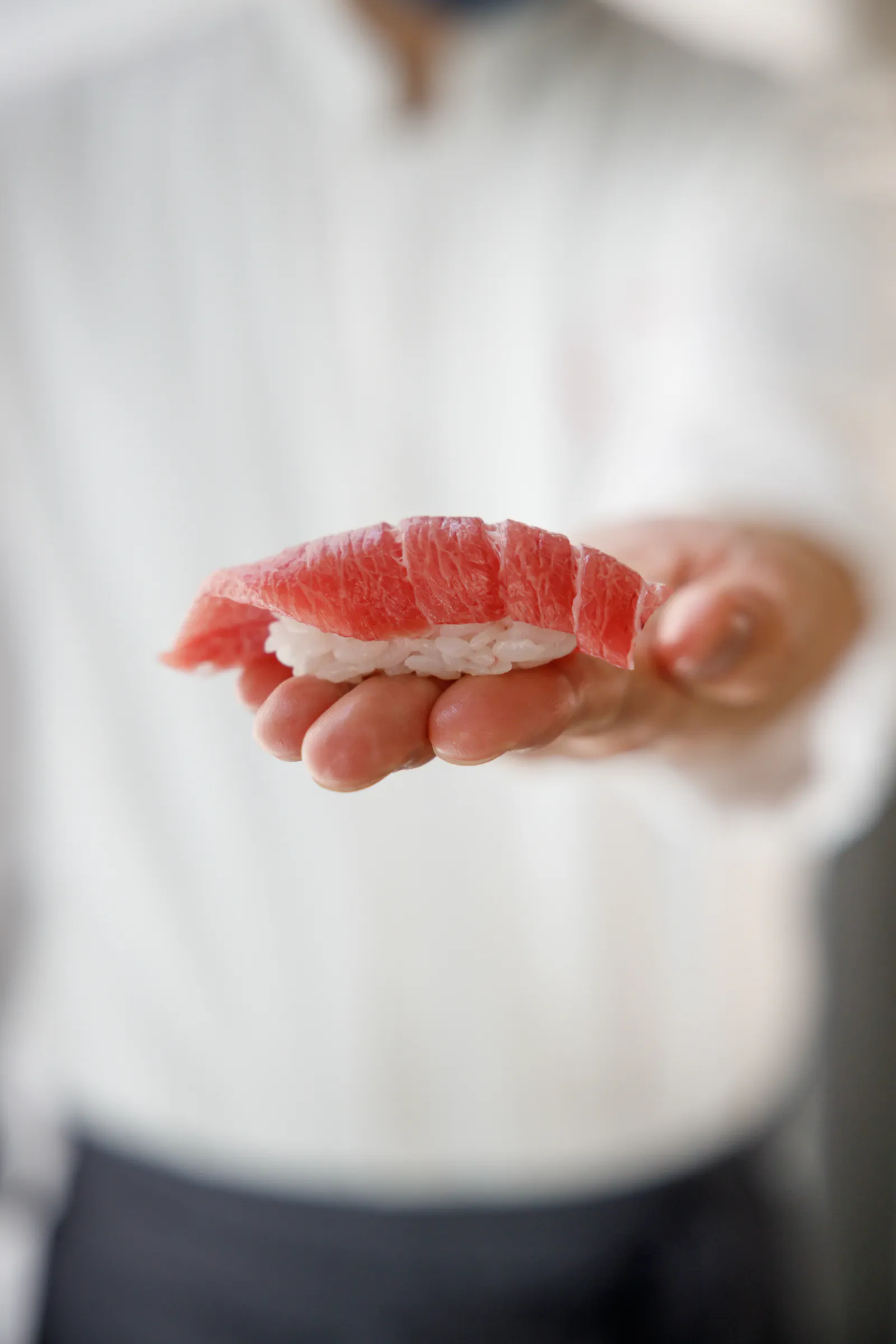 Hand presenting a piece of tuna nigiri sushi