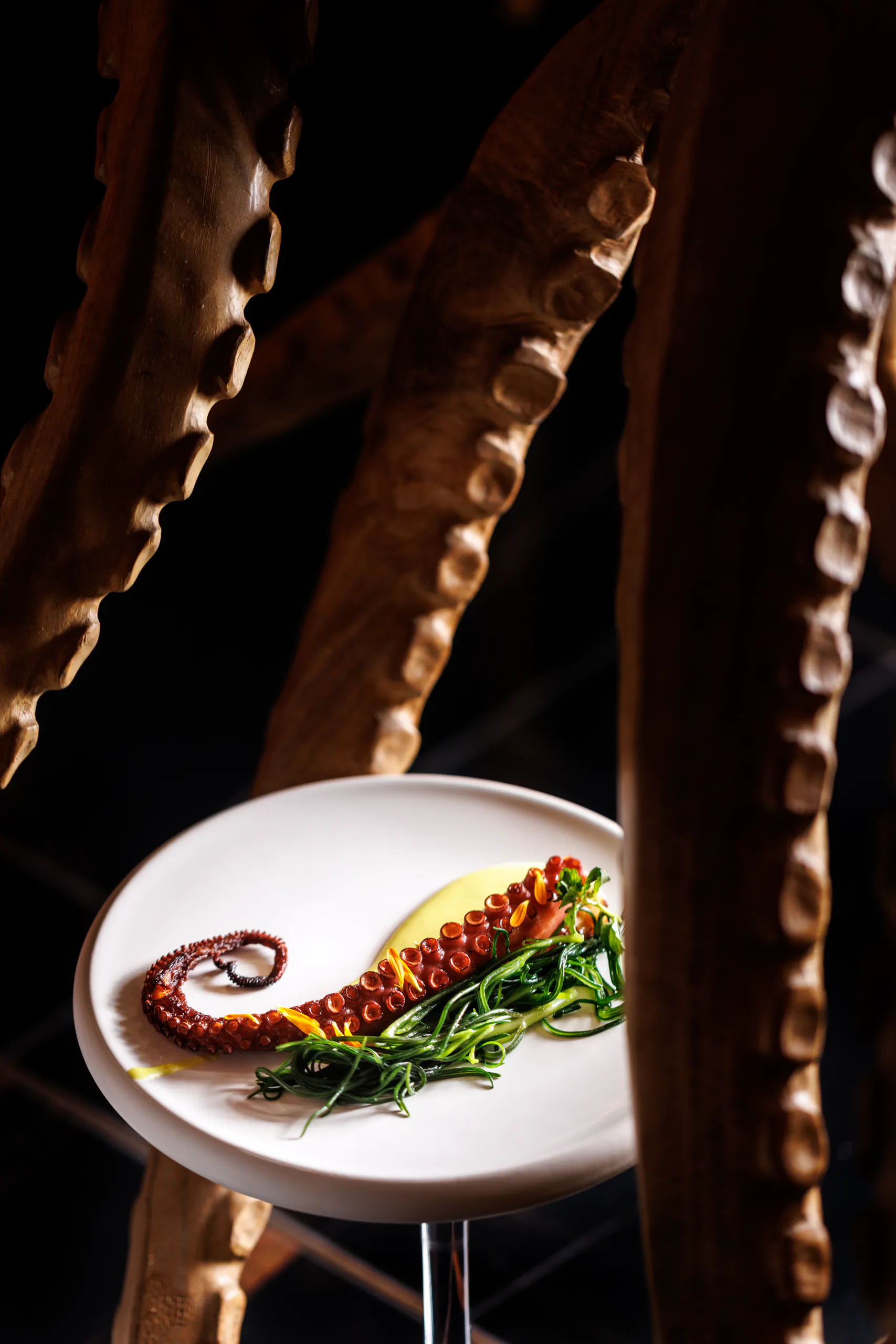 Charred octopus tentacle with greens on a pedestal plate