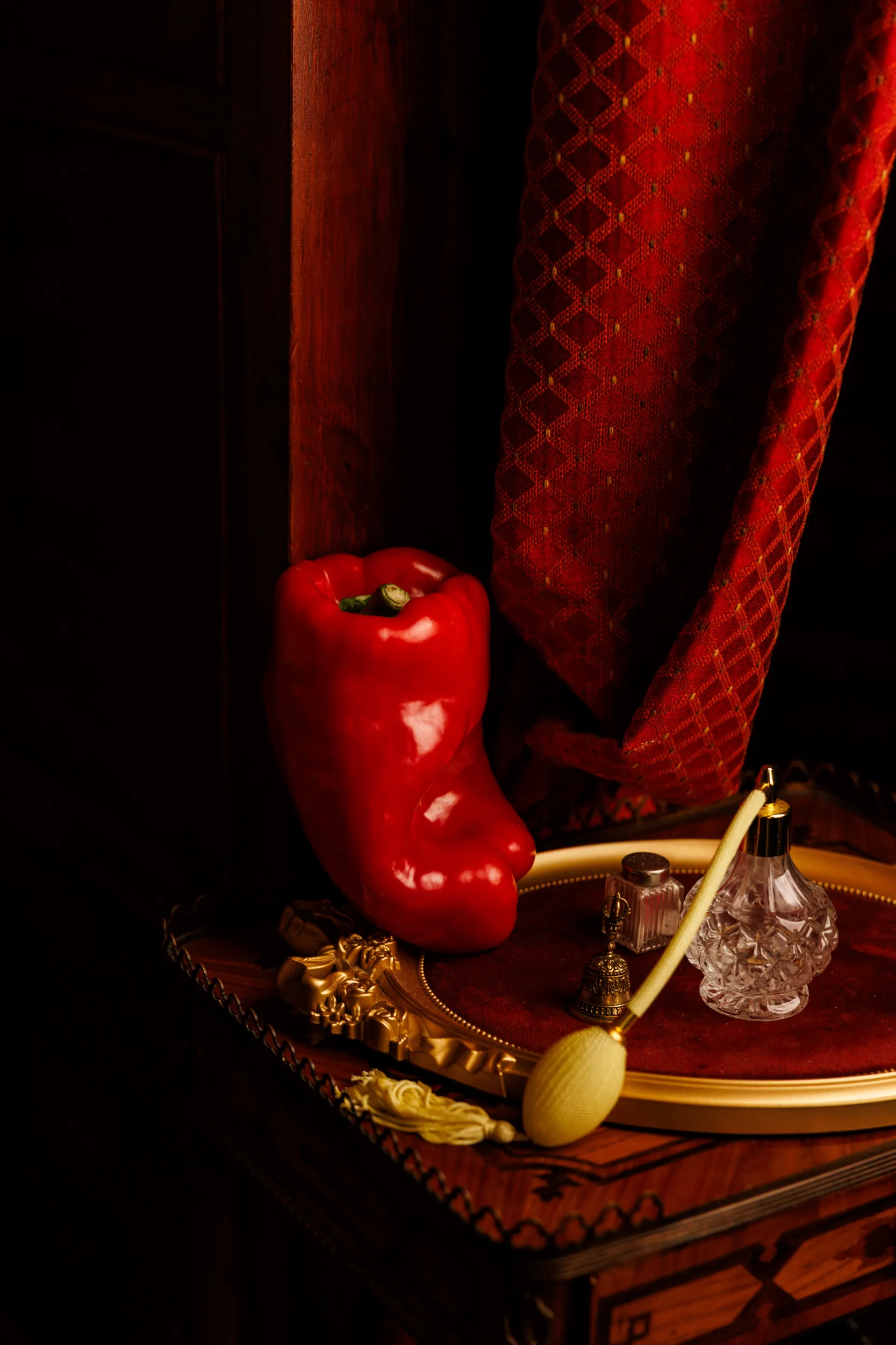 Red bell pepper on an ornate gold tray against red velvet, editorial still life
