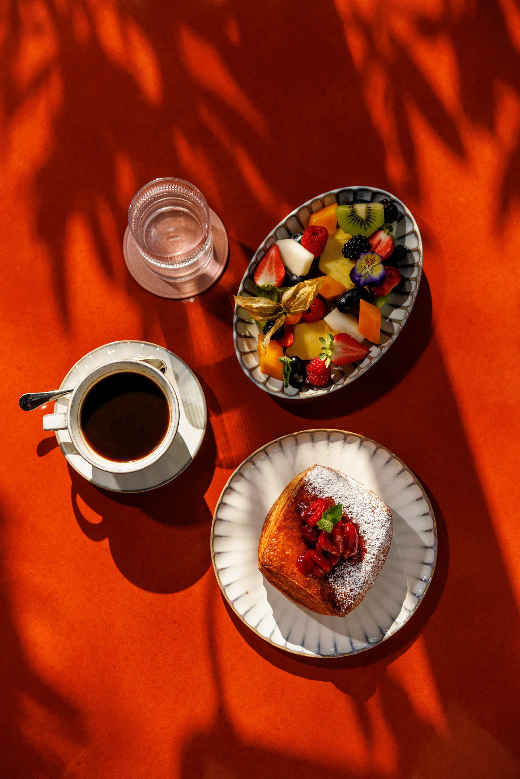 Breakfast of coffee, fruit and pastry on an orange backdrop - The Wilde, Milan, Italy