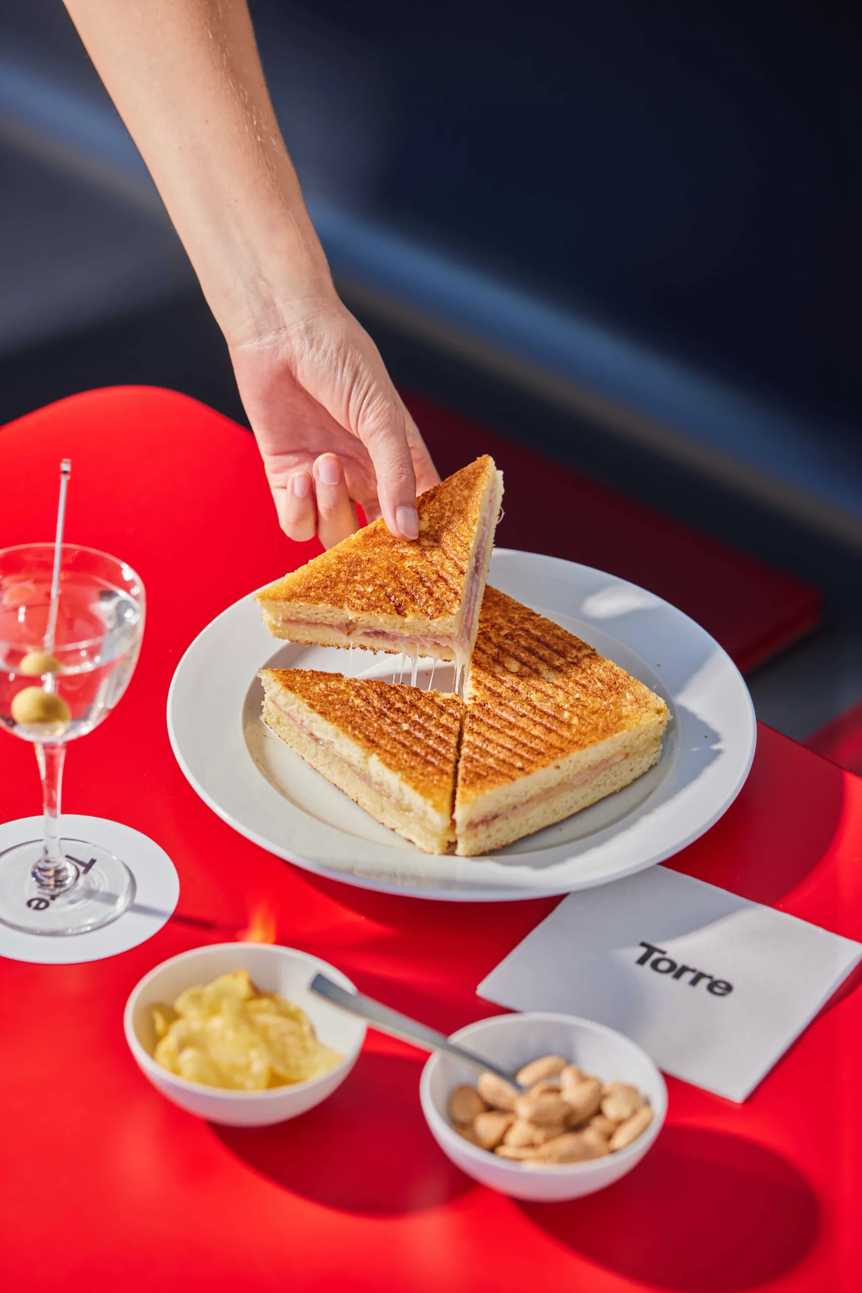Hand lifting a slice of toasted sandwich beside a martini - Torre, Milan, Italy