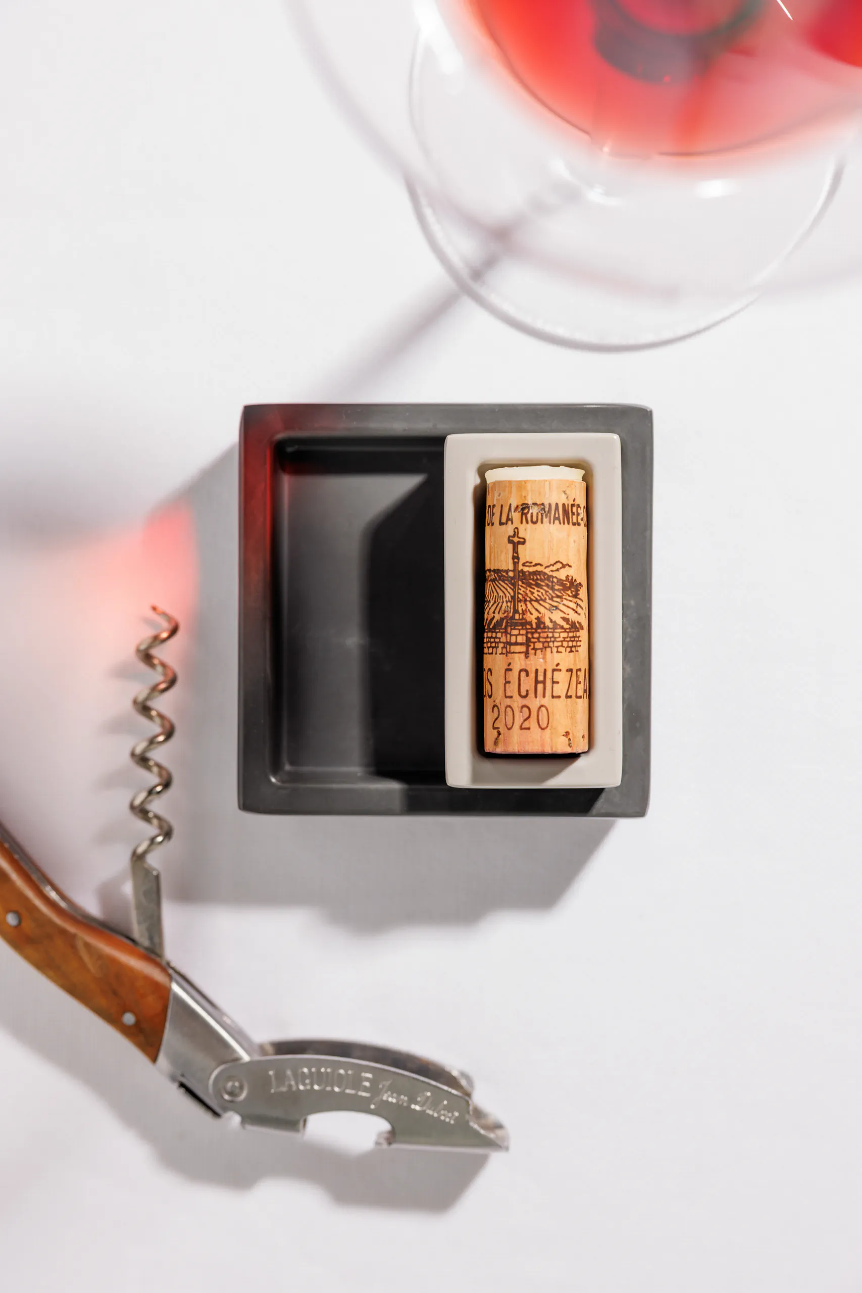 Overhead view of a corkscrew and a wine cork on a white surface