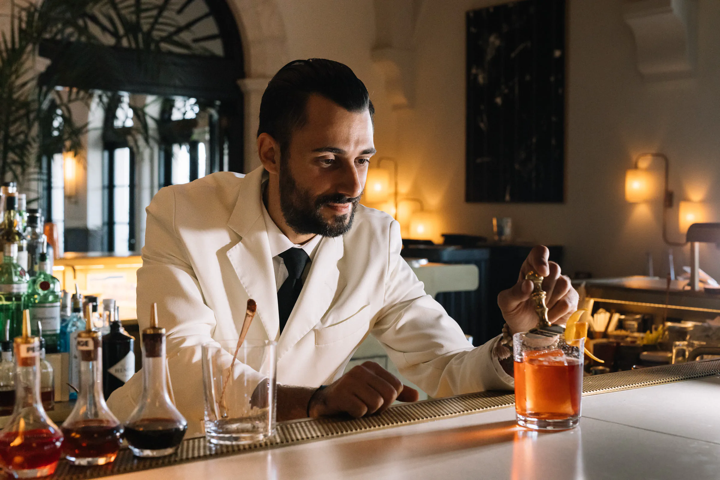 Bartender in a white jacket garnishing a cocktail at an elegant hotel bar