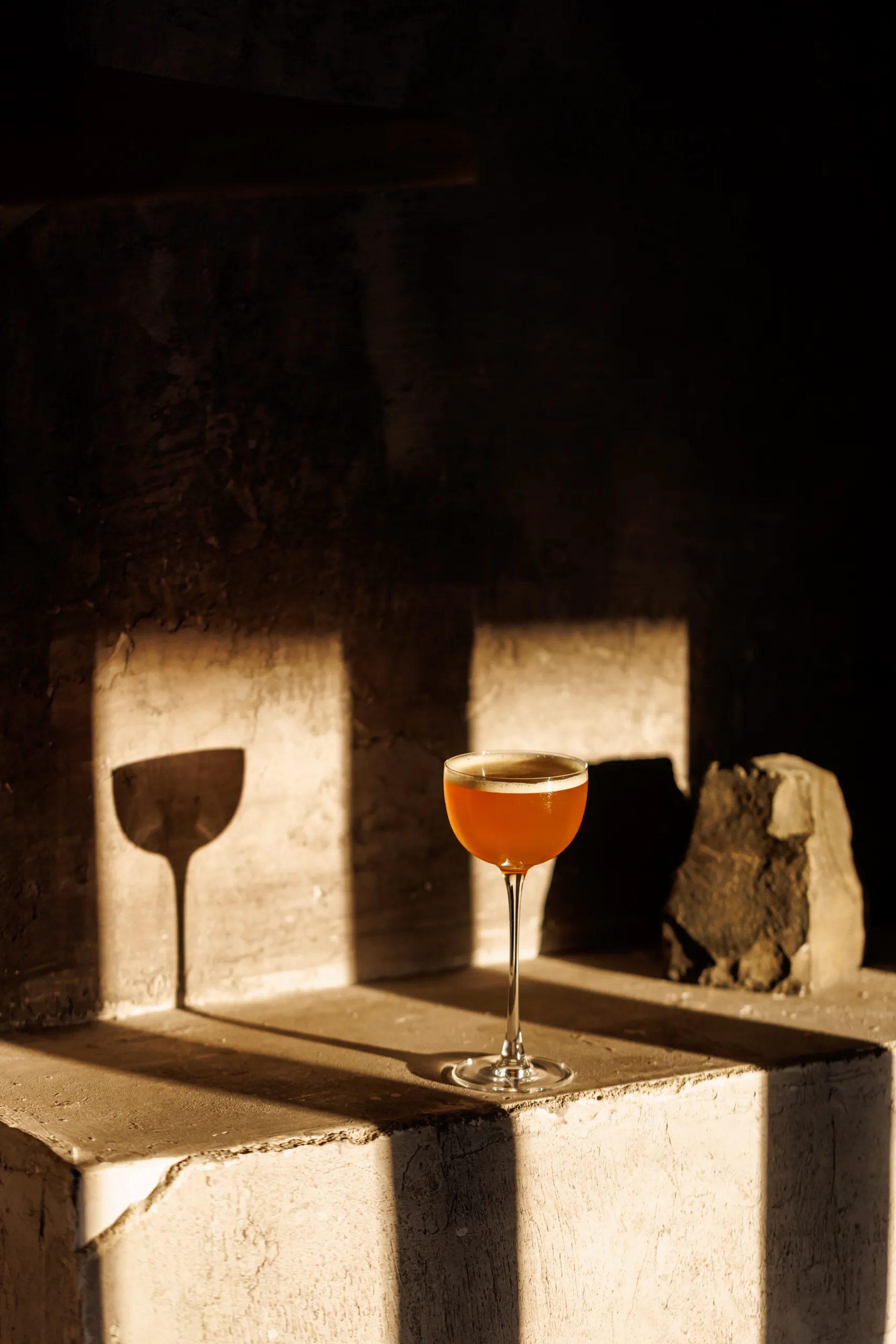 Two cocktail glasses on stone blocks lit by a shaft of warm sunlight