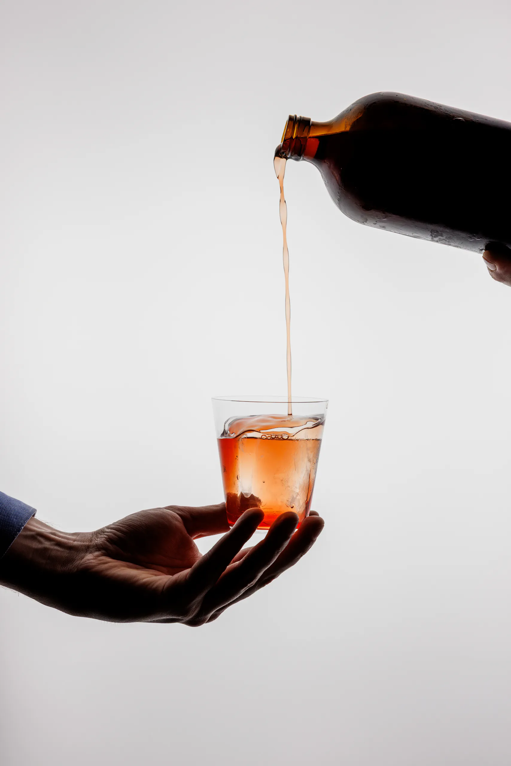 Amber liquid being poured from a bottle into a glass held in a hand