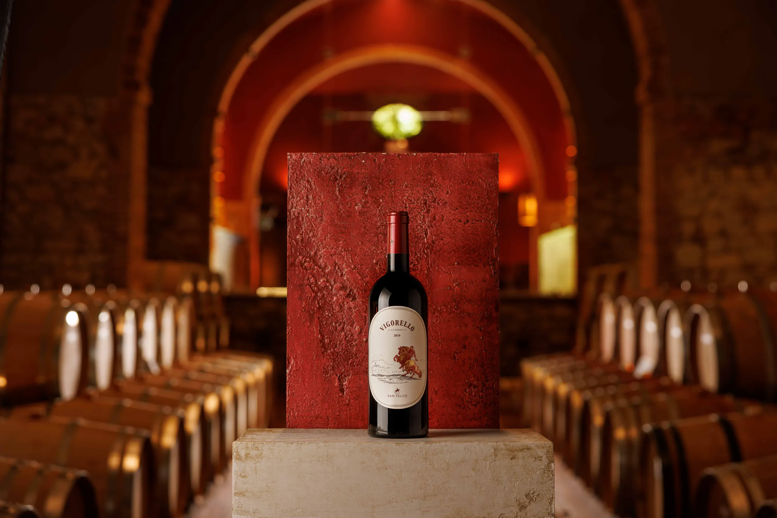 Bottle of red wine on a plinth in an arched wine cellar lined with barrels - San Felice Winery, Chianti, Tuscany, Italy