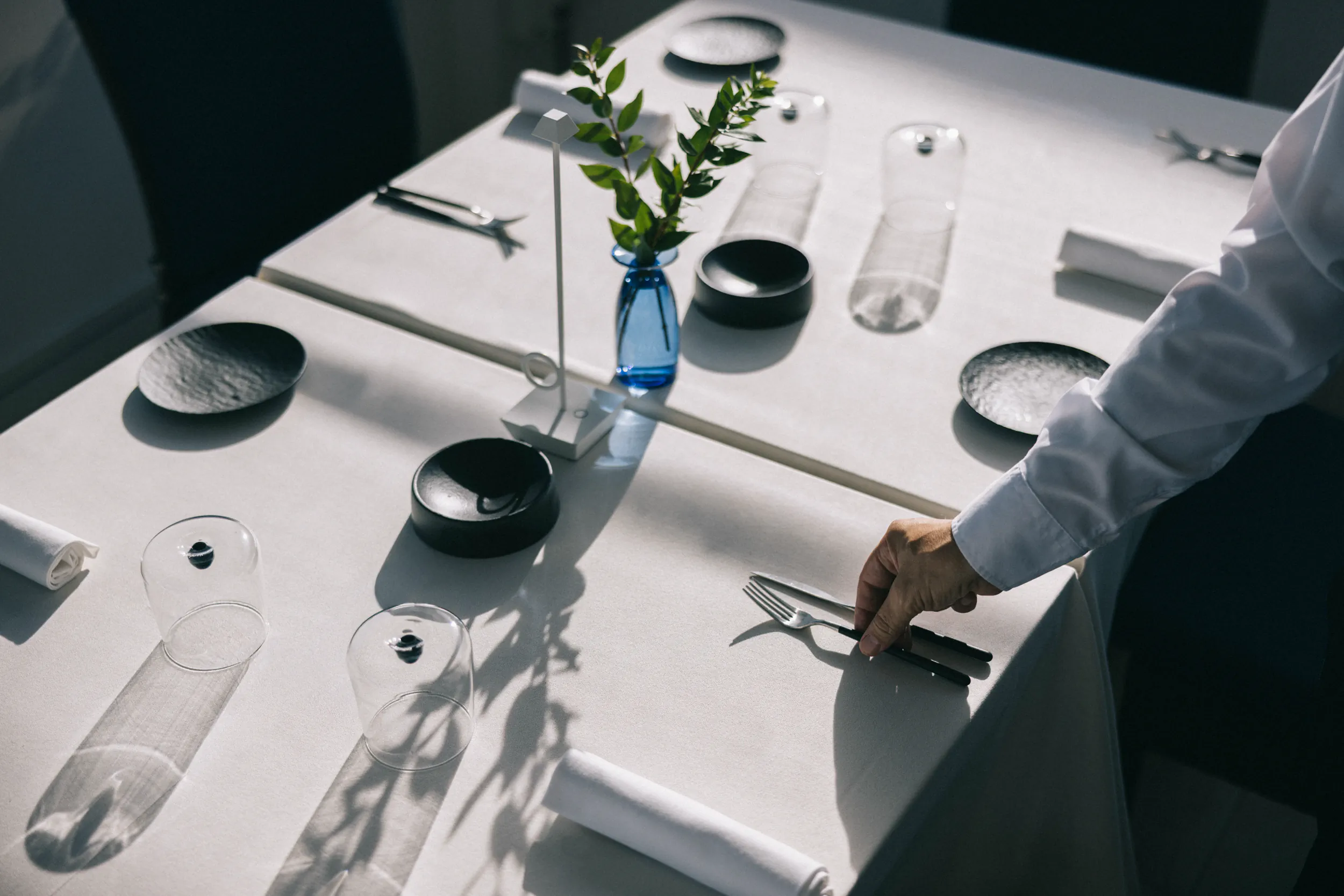 Table set with plates, glasses and a small vase, a waiter adjusting the cutlery