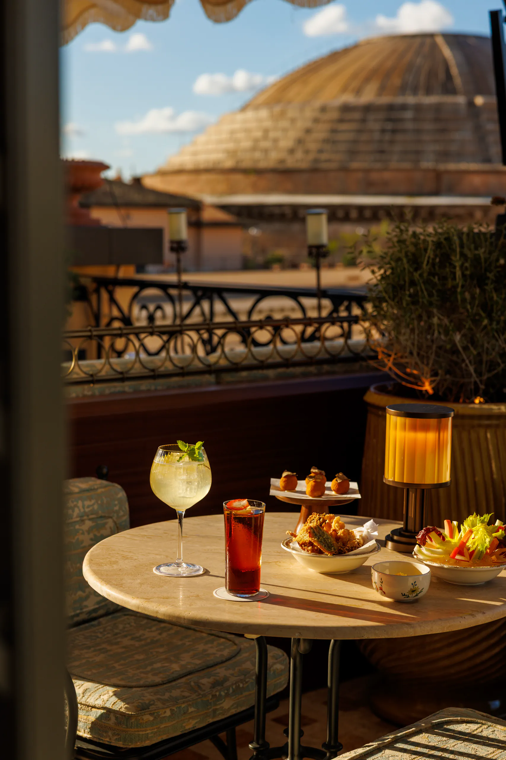 Rooftop table set with cocktails and small bites overlooking a city dome at dusk