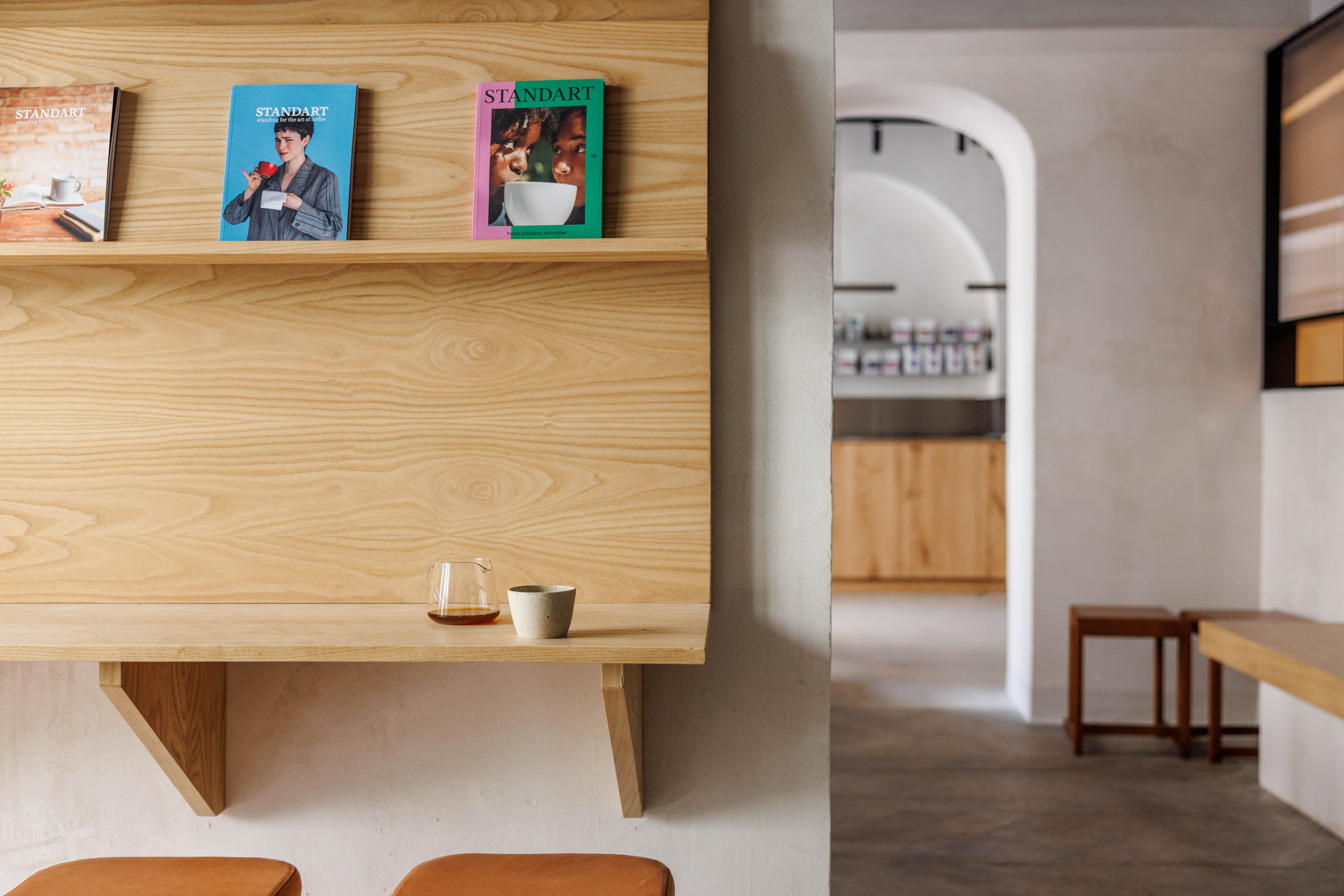 Minimalist wood-panelled interior with a floating shelf, cups and a wooden stool