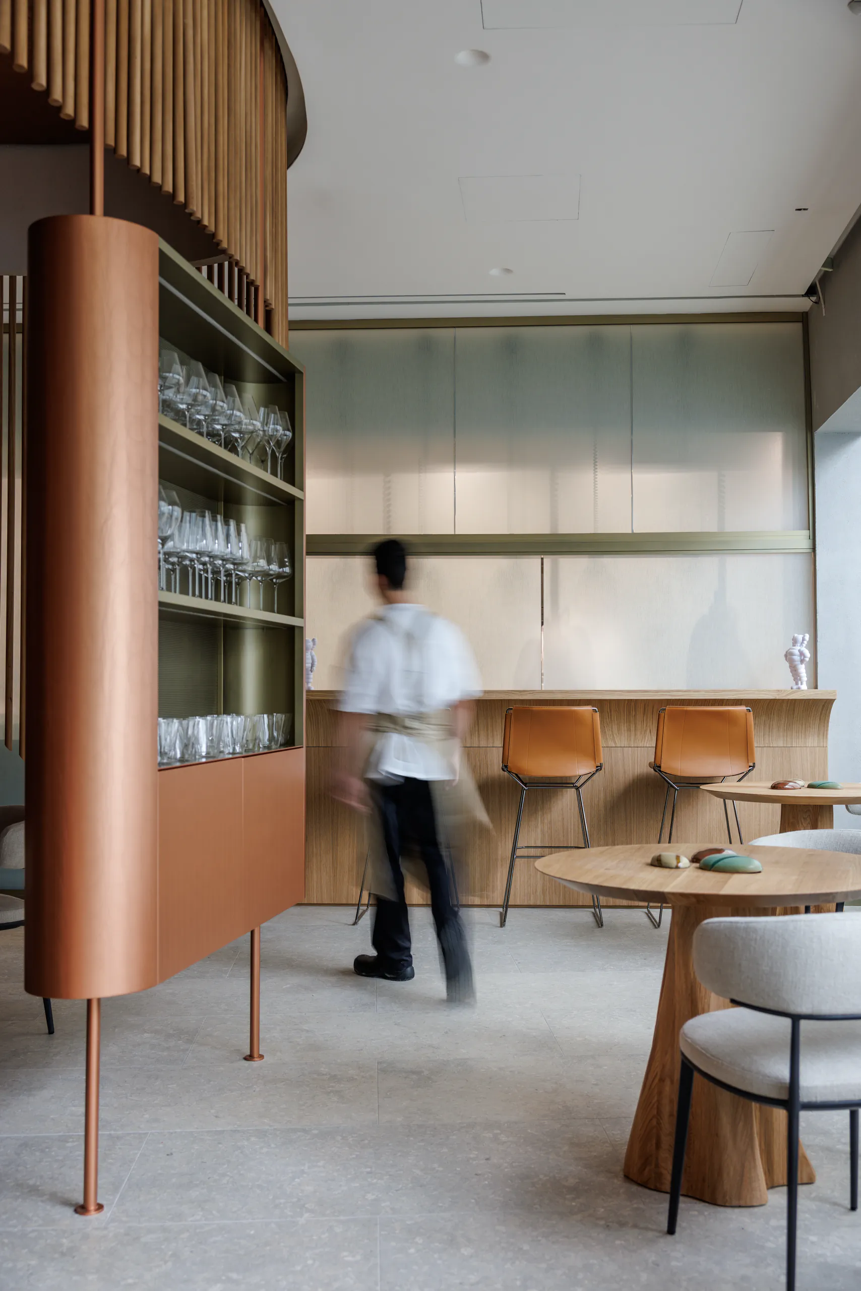 Minimalist restaurant interior with a curved wooden counter and a person walking