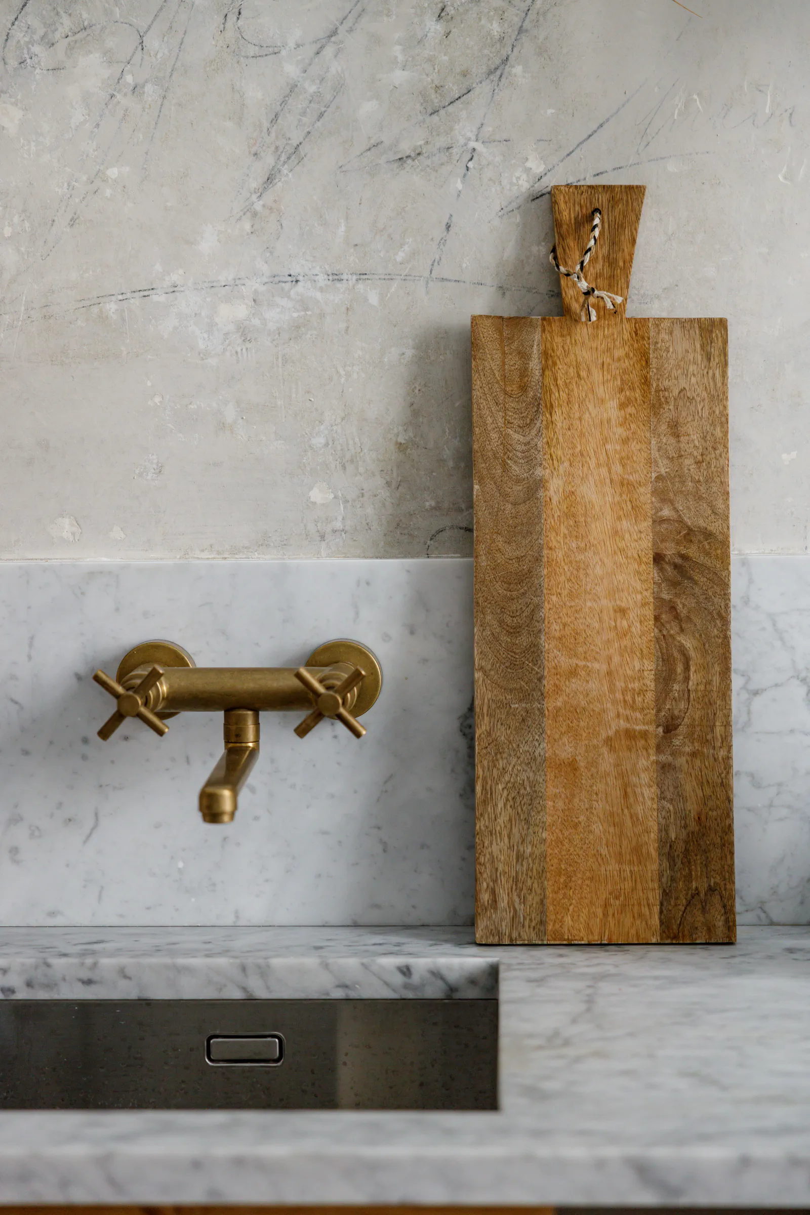 Brass wall-mounted tap over a marble basin with a wooden board