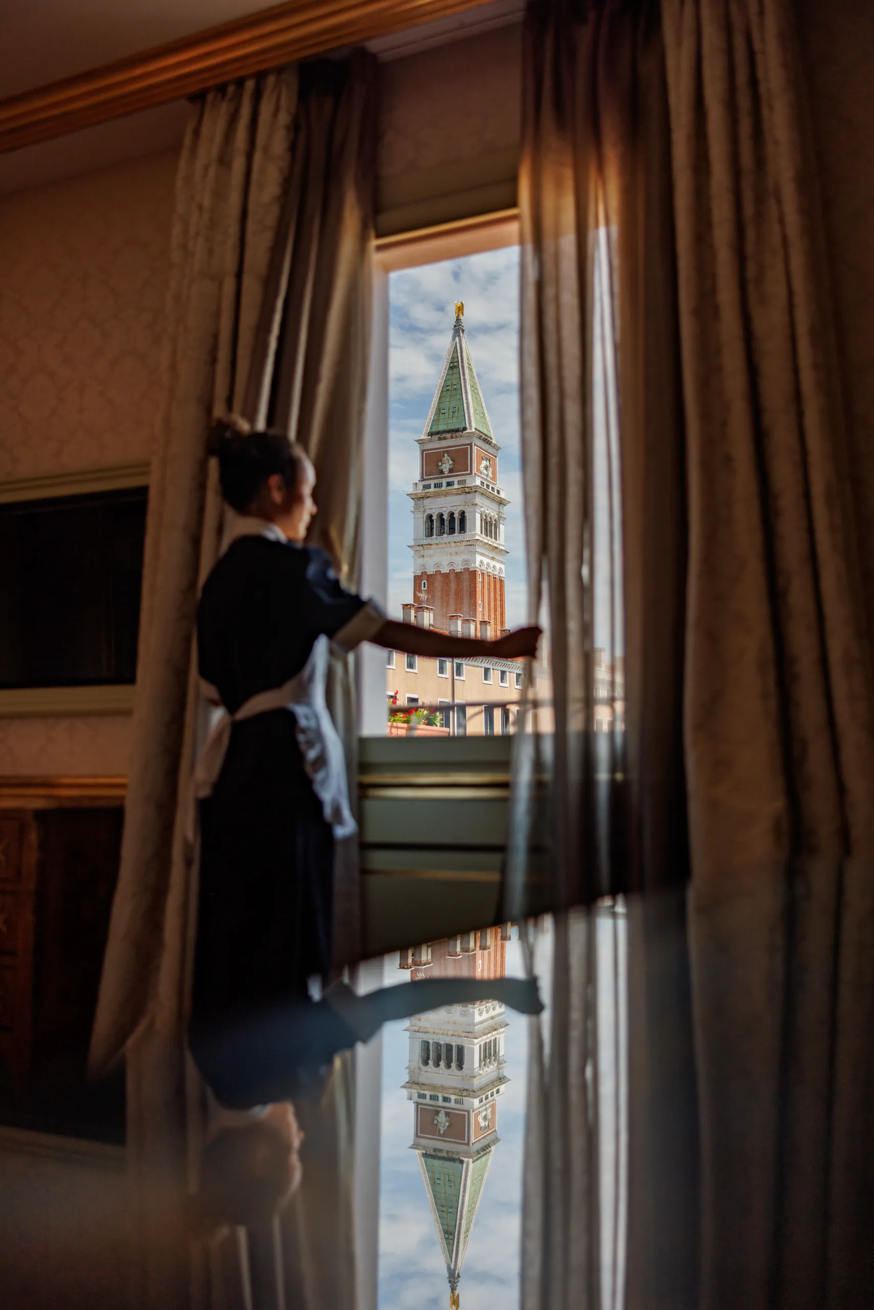 Dimly lit room with framed pictures and a person by a curtained window