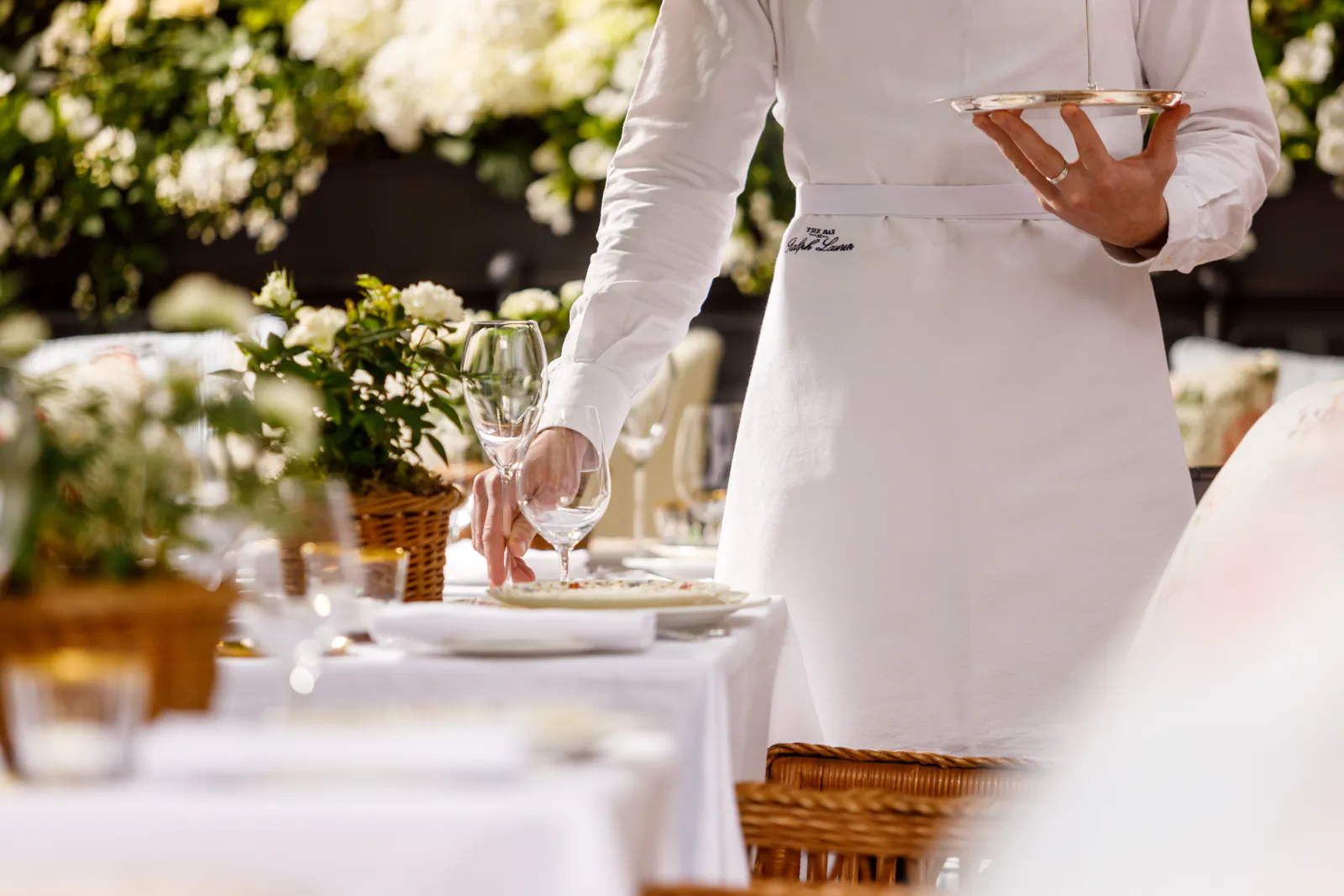Waiter in white setting an elegant table with flowers and fine tableware