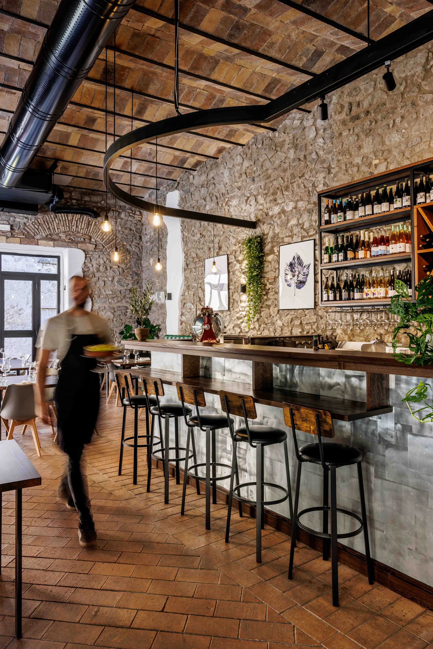 Bistro interior with a long counter, high stools and shelves of bottles