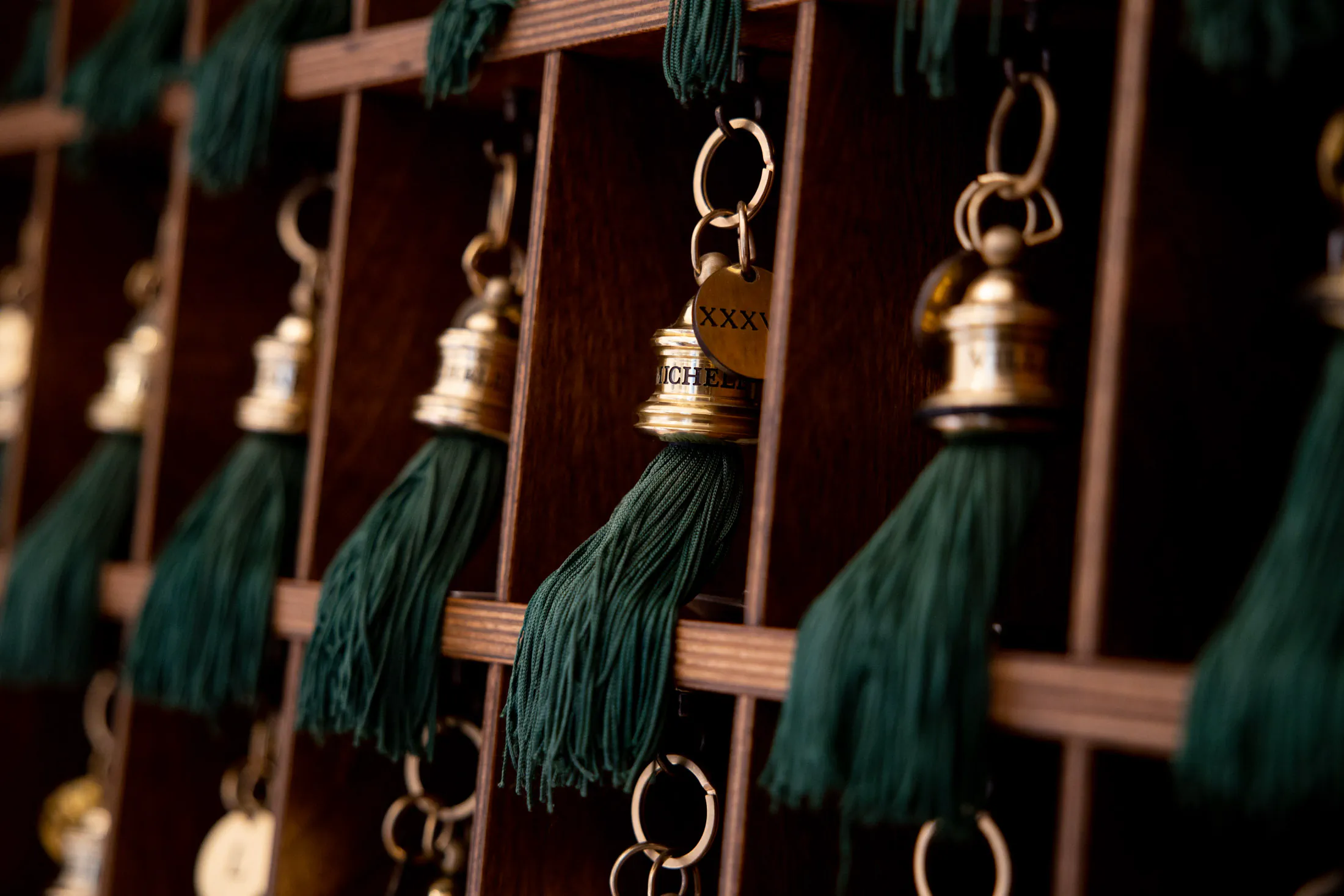 Row of hotel room keys with green tassels on a wooden key rack