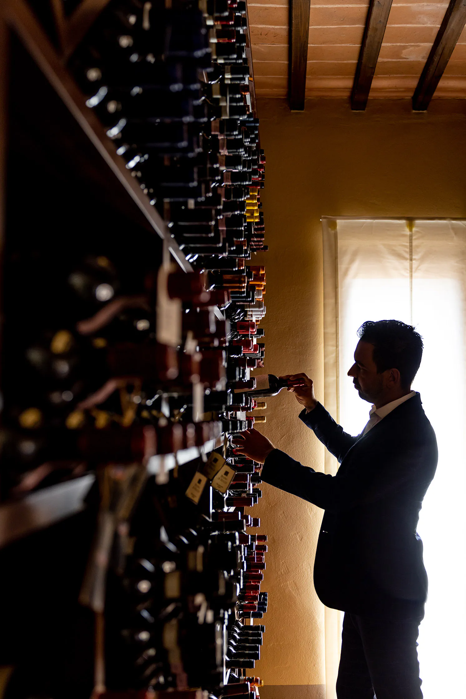 Person in a suit selecting a bottle from a backlit wine wall