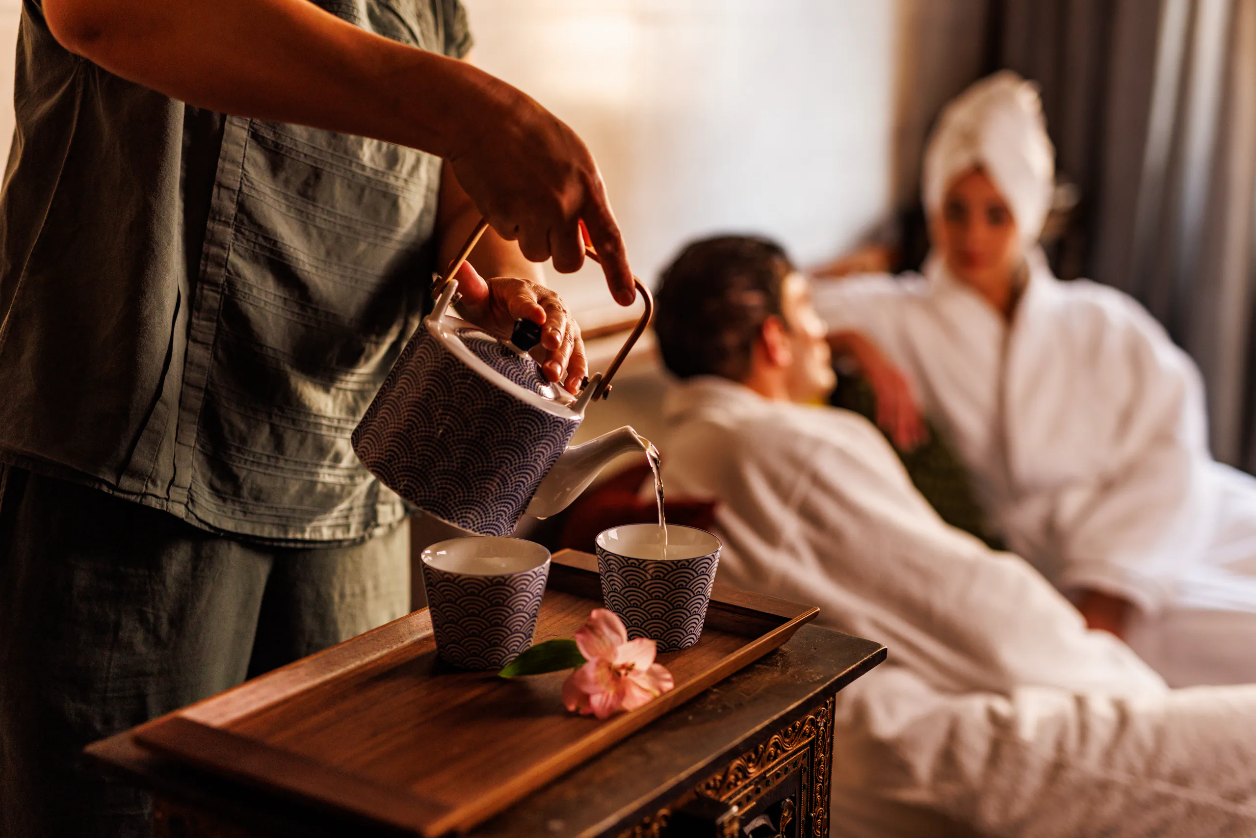 Attendant pouring tea while guests in robes relax at a spa