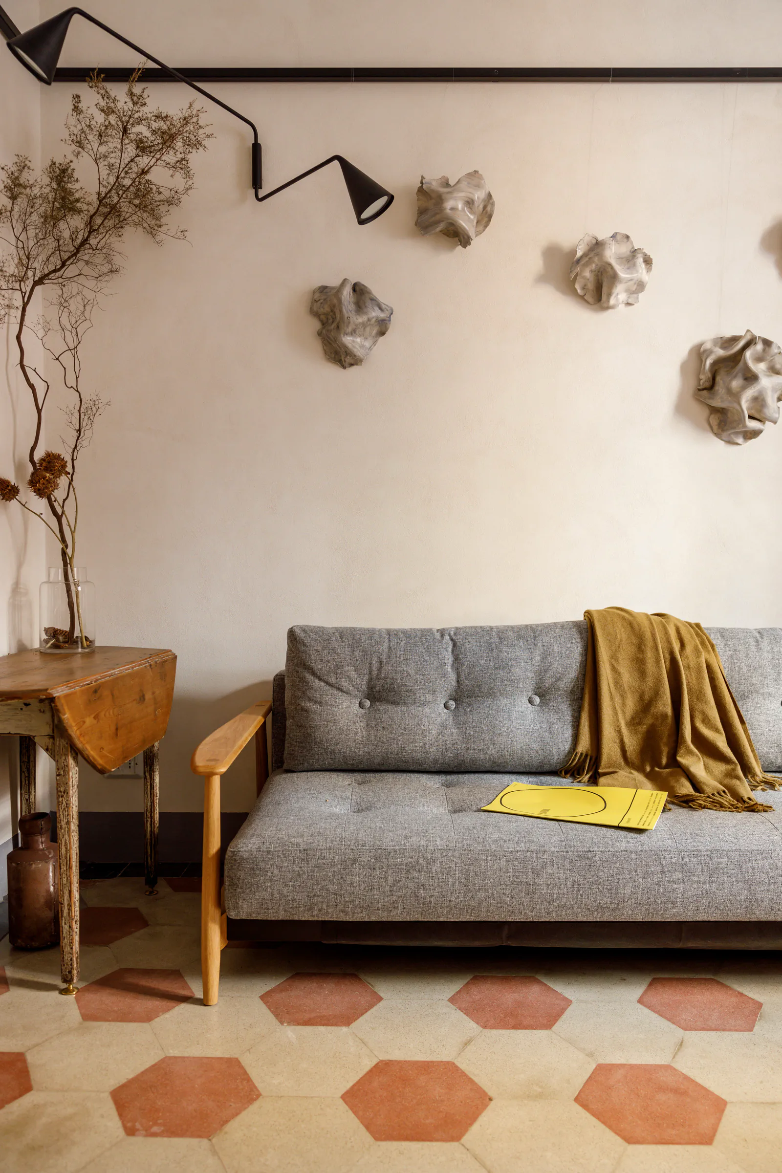 Living area with a grey sofa, a draped throw and dried flowers on the wall