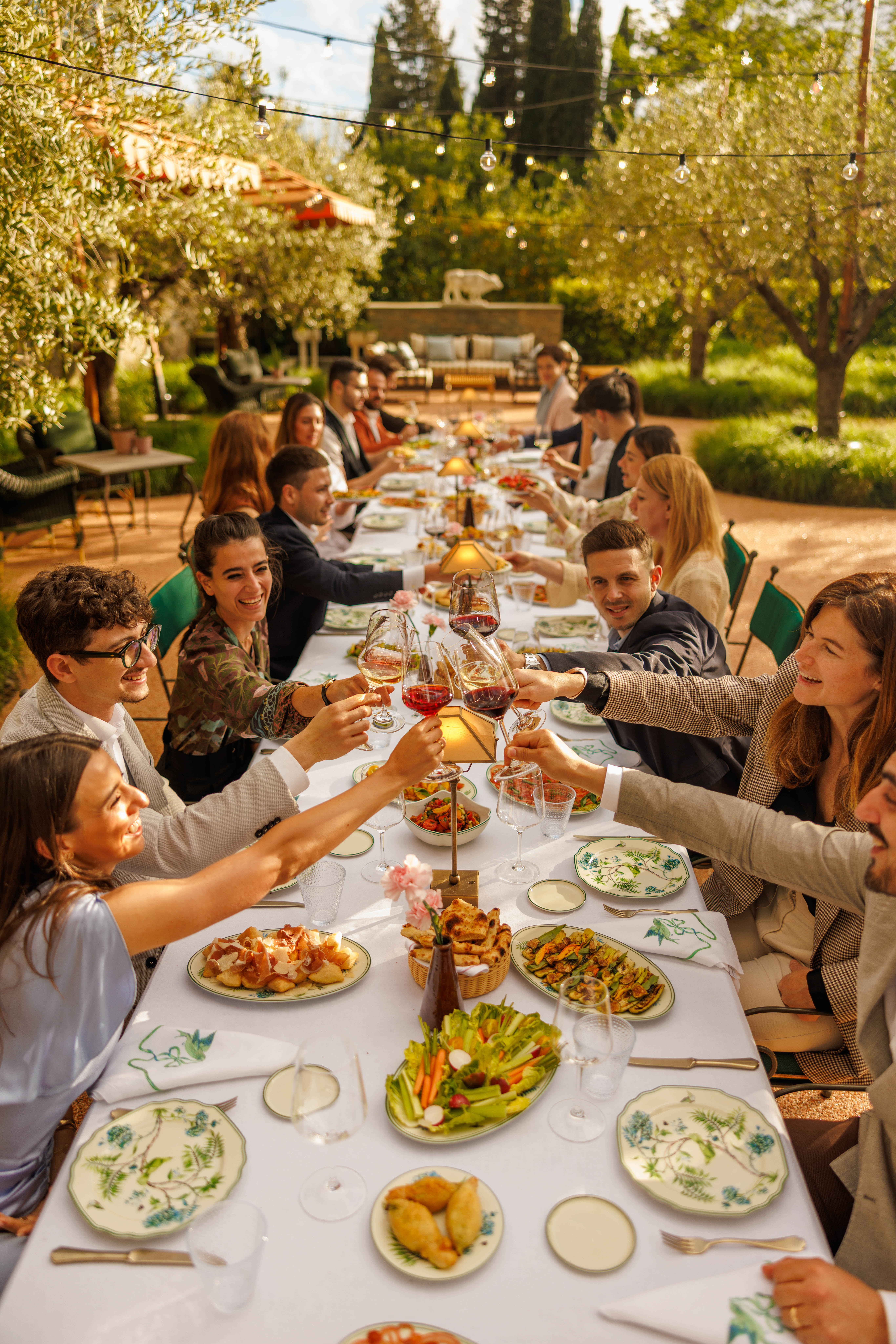 Long banquet table set outdoors in a garden with guests toasting