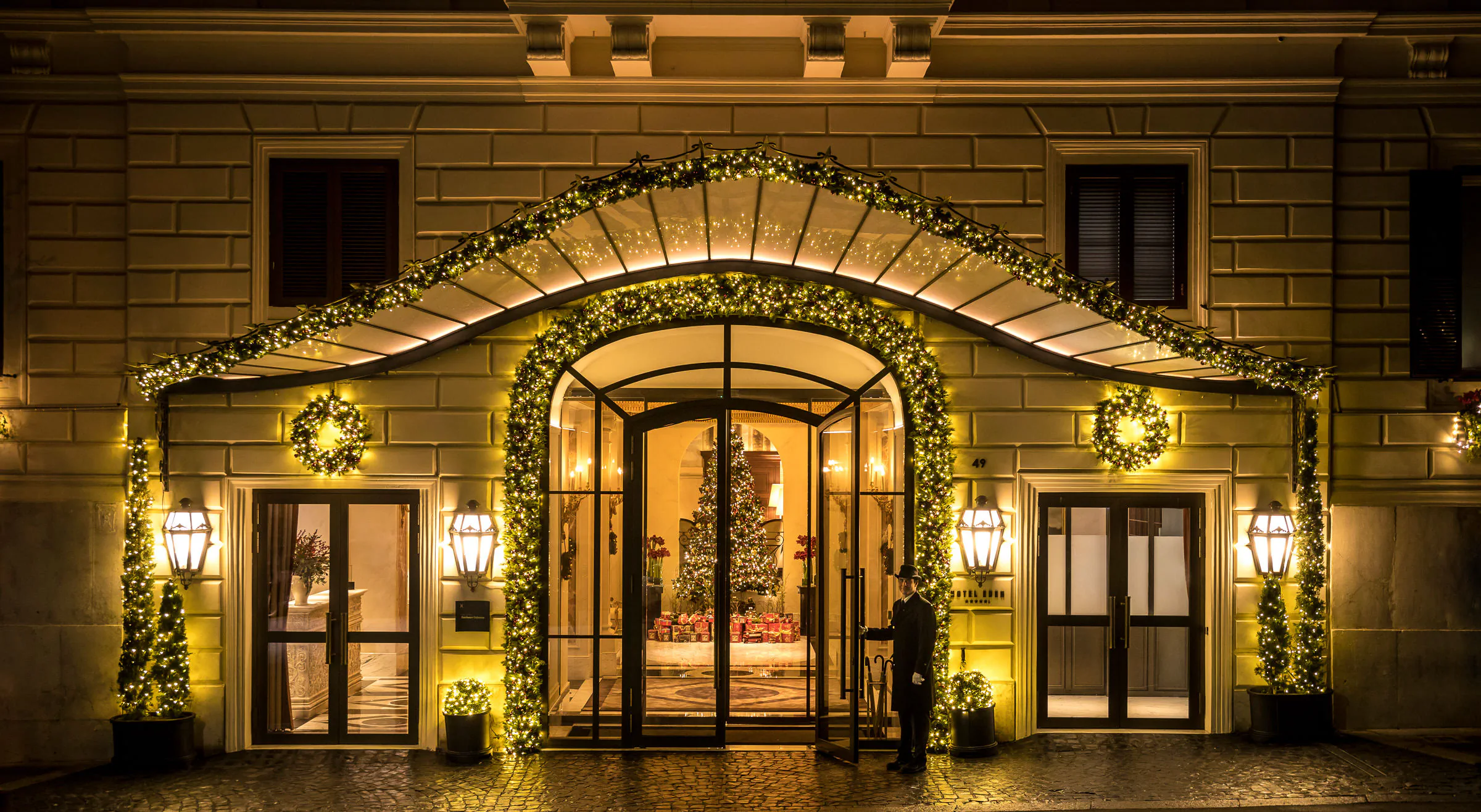 Illuminated hotel entrance at night with an arched facade decorated with greenery