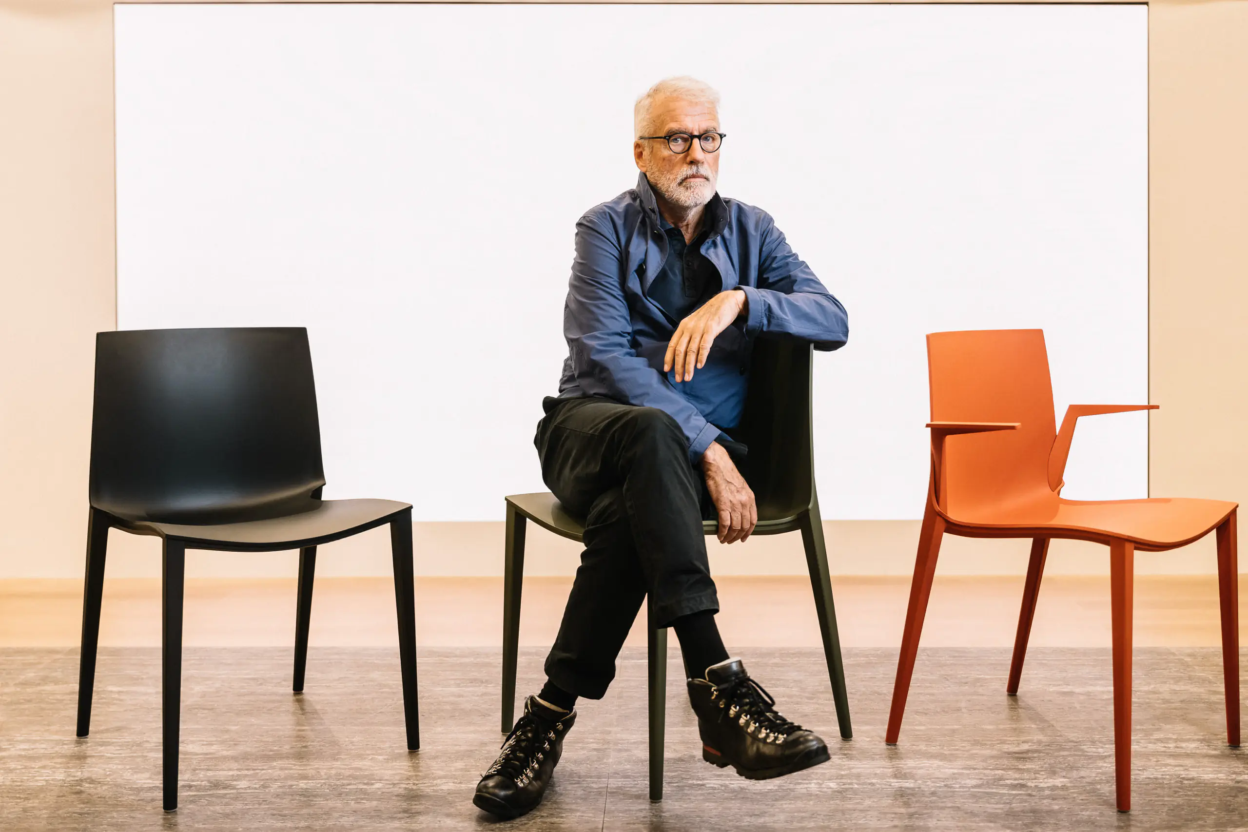 Older man in a denim shirt seated among modern chairs