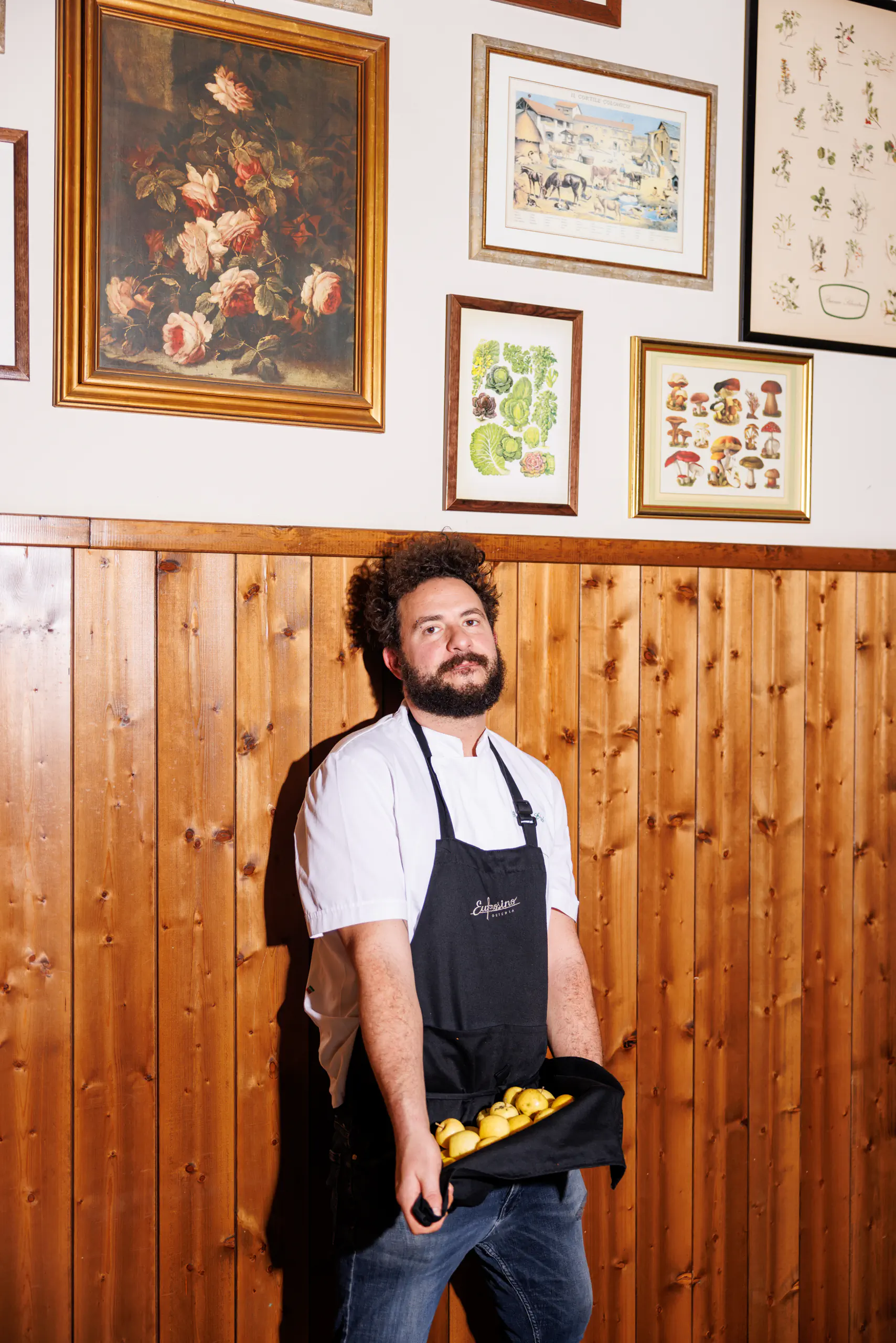 Man in an apron in a wood-panelled room with framed pictures