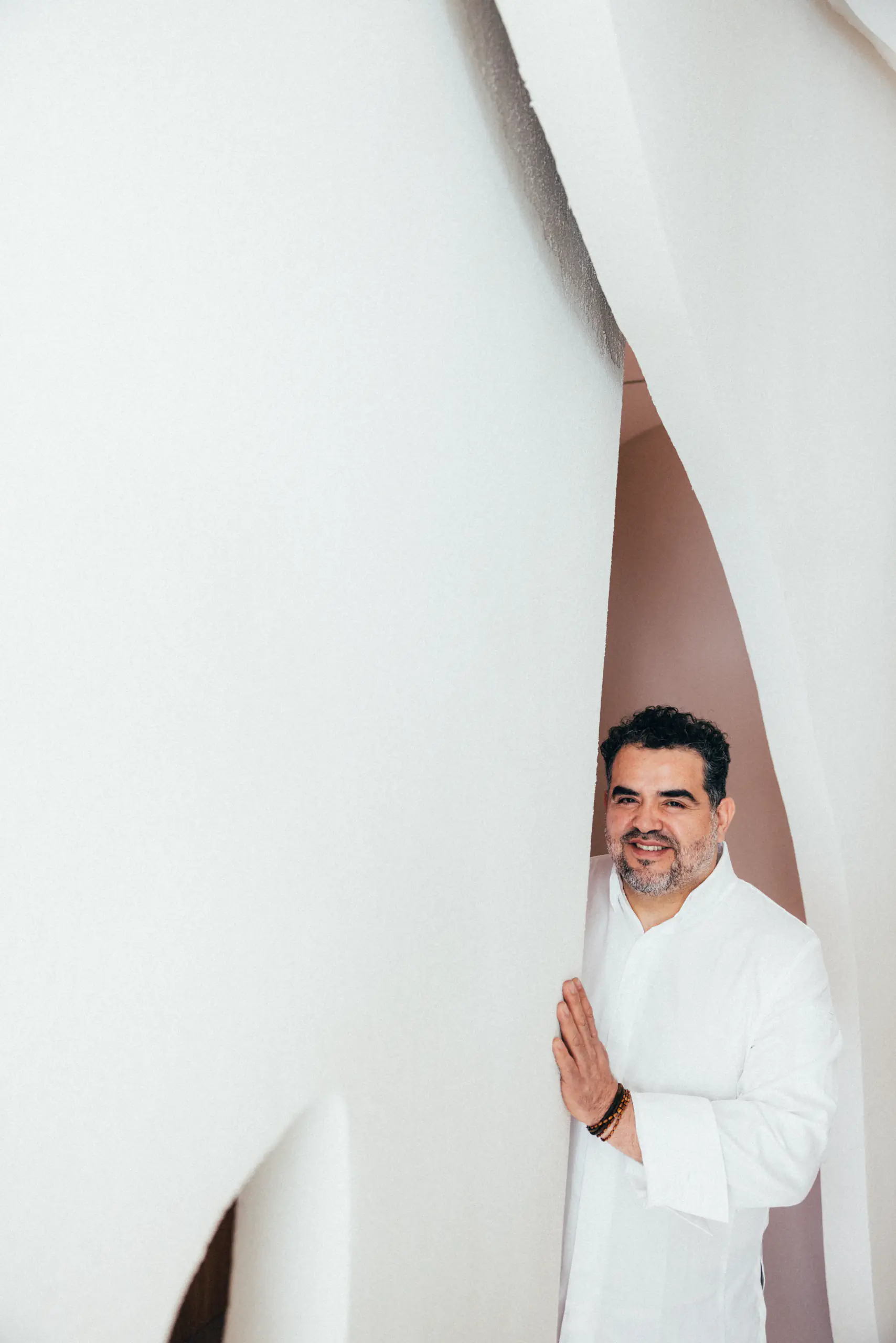 Man in whites peeking from behind a white curved wall
