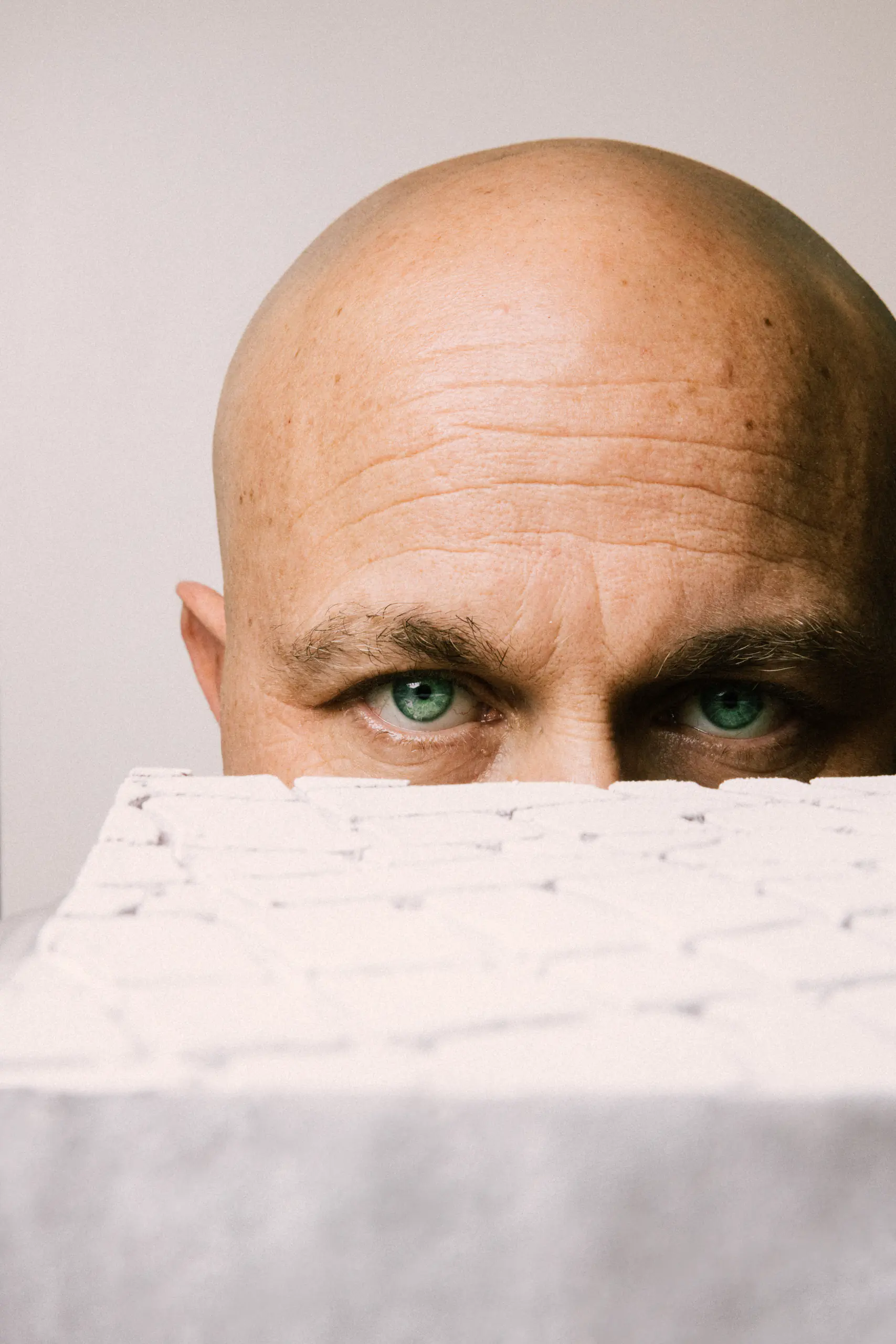 Bald man peeking over a white textured surface